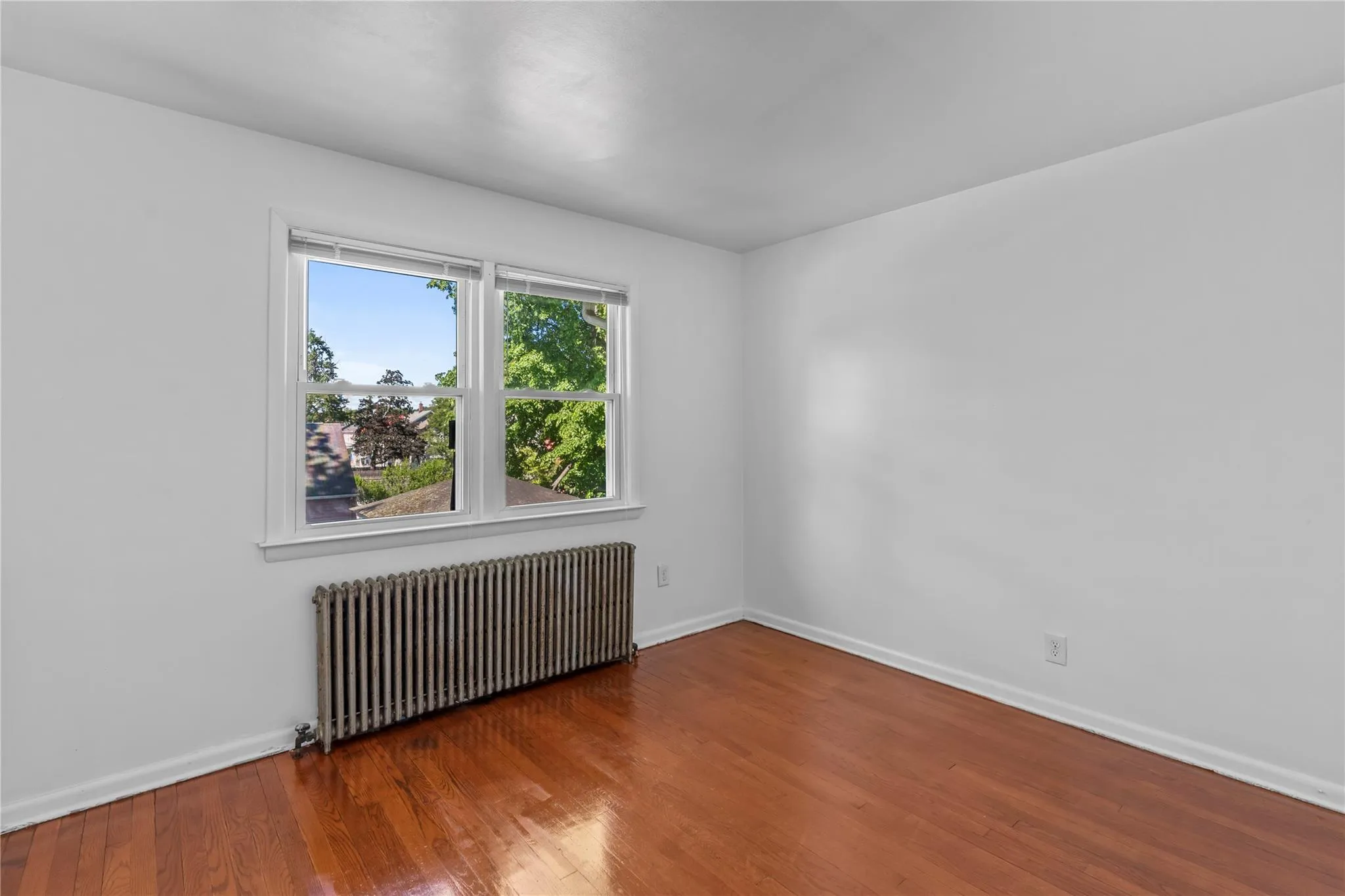 Spare room with radiator, wood finished floors, and baseboards Spare room with radiator, wood finished floors, and baseboards