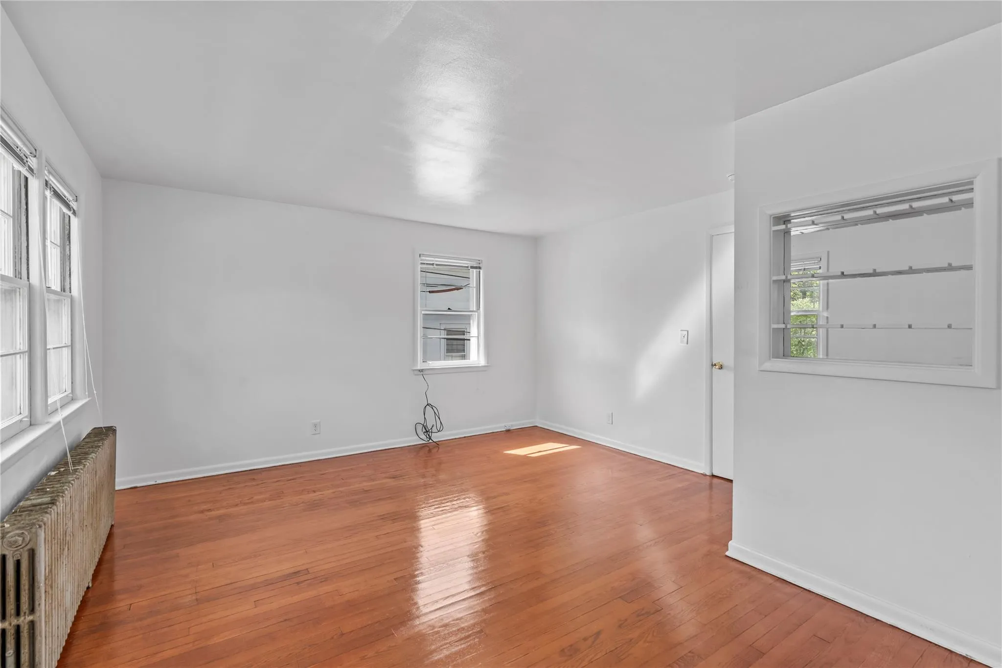 Unfurnished room with radiator, wood-type flooring, and baseboards Unfurnished room with radiator, wood-type flooring, and baseboards