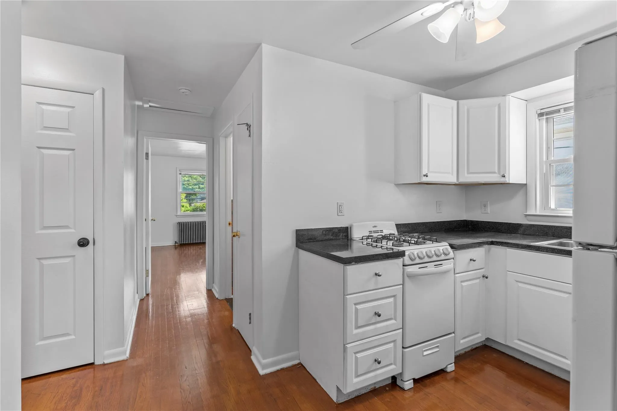 Kitchen with white appliances, radiator heating unit, white cabinets, dark countertops, and dark wood finished floors Kitchen with white appliances, radiator heating unit, white cabinets, dark countertops, and dark wood finished floors