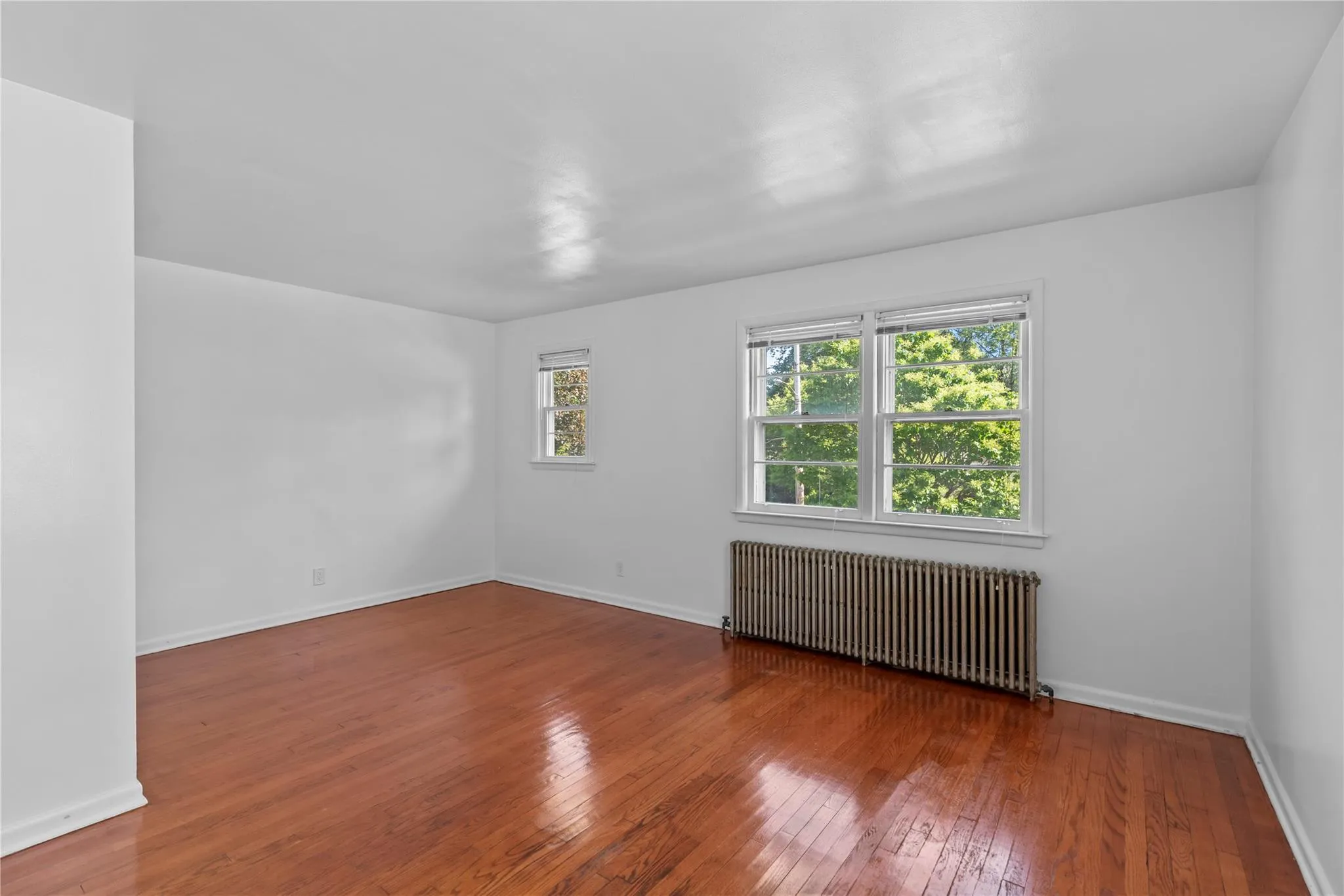 Empty room with radiator heating unit, hardwood / wood-style floors, and baseboards Empty room with radiator heating unit, hardwood / wood-style floors, and baseboards