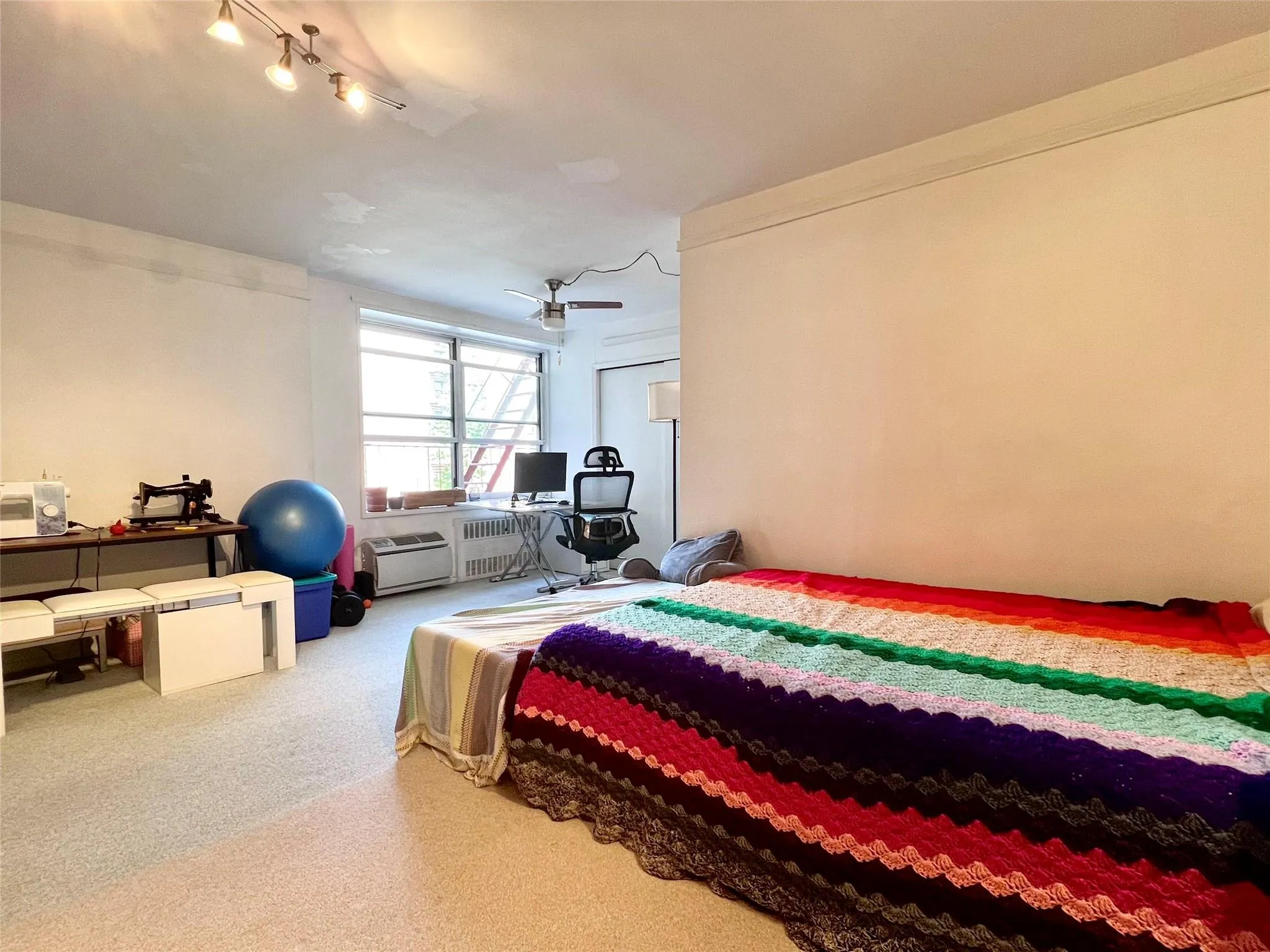 Carpeted bedroom featuring track lighting, a ceiling fan, and radiator heating unit Carpeted bedroom featuring track lighting, a ceiling fan, and radiator heating unit