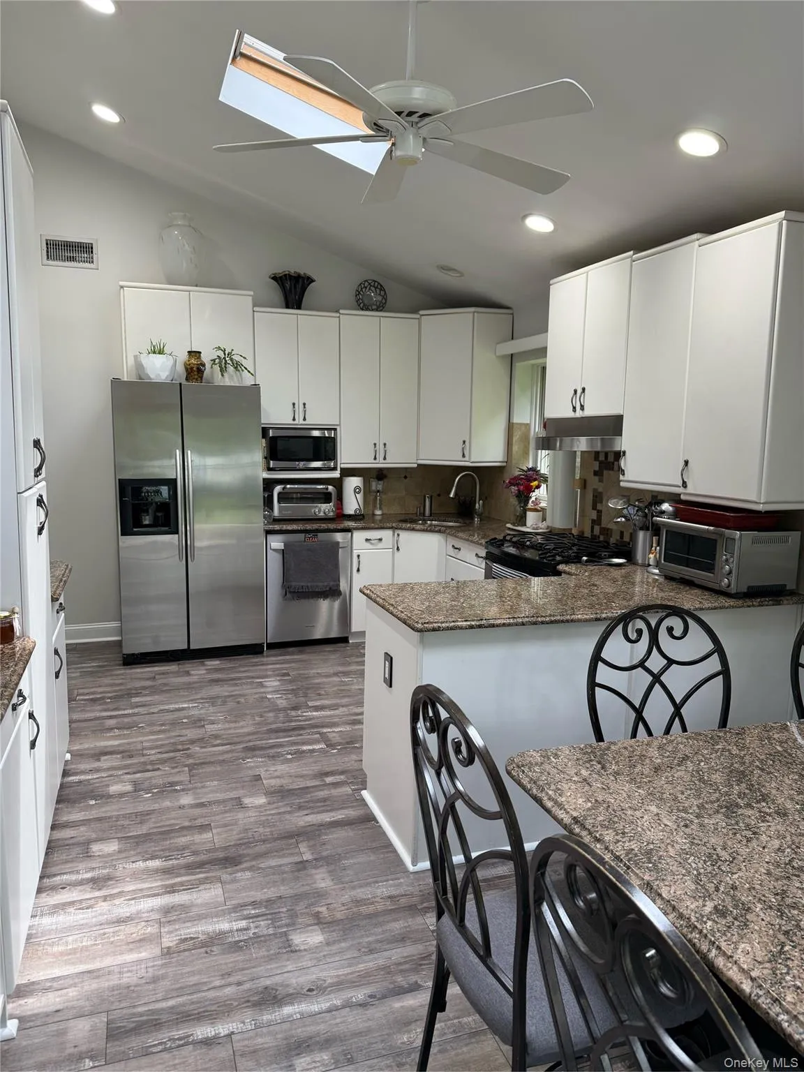 Kitchen featuring appliances with stainless steel finishes, lofted ceiling, ceiling fan, a peninsula, and wood finished floors Kitchen featuring appliances with stainless steel finishes, lofted ceiling, ceiling fan, a peninsula, and wood finished floors