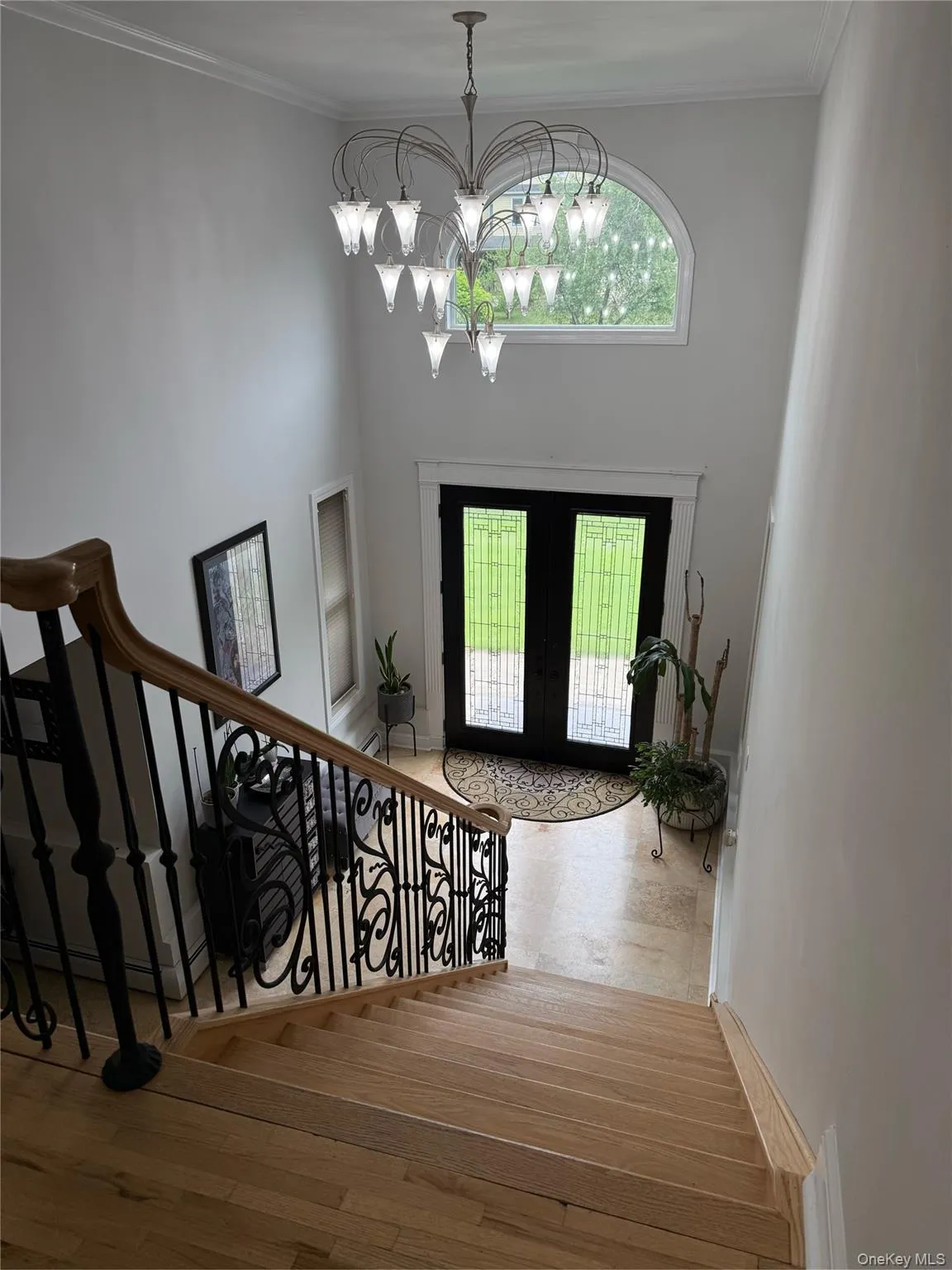 Entrance foyer with french doors, stairway, a chandelier, wood finished floors, and crown molding Entrance foyer with french doors, stairway, a chandelier, wood finished floors, and crown molding