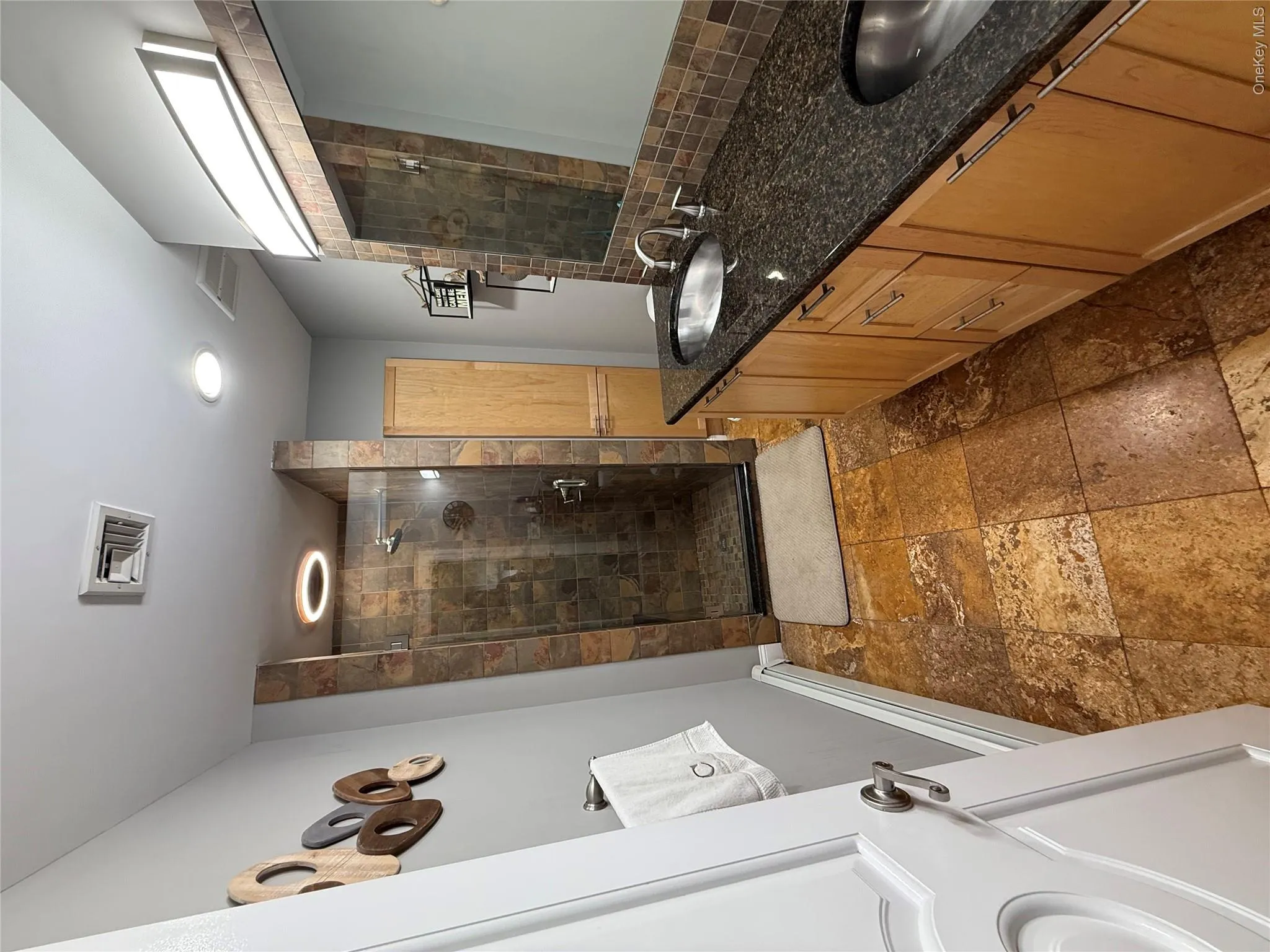 Bathroom with a shower stall, stone tile floors, double vanity, baseboards, and baseboard heating Bathroom with a shower stall, stone tile floors, double vanity, baseboards, and baseboard heating