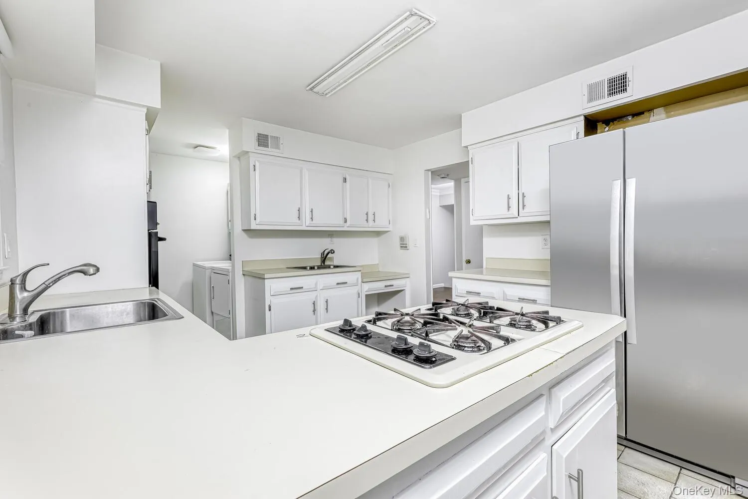 Kitchen featuring stainless steel refrigerator, a sink, washing machine and dryer, and white gas stovetop Kitchen featuring stainless steel refrigerator, a sink, washing machine and dryer, and white gas stovetop