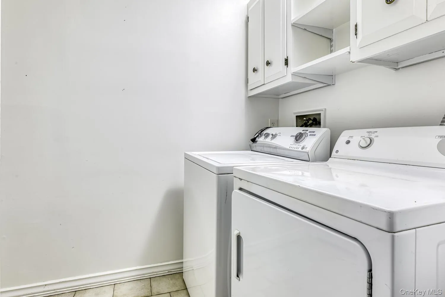 Laundry room with washing machine and dryer, cabinet space, light tile patterned flooring, and baseboards Laundry room with washing machine and dryer, cabinet space, light tile patterned flooring, and baseboards