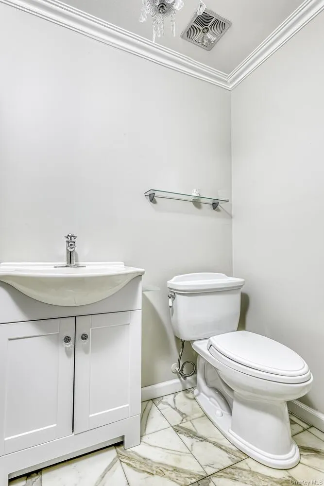 Bathroom with toilet, marble look tiles, vanity, baseboards, and crown molding Bathroom with toilet, marble look tiles, vanity, baseboards, and crown molding