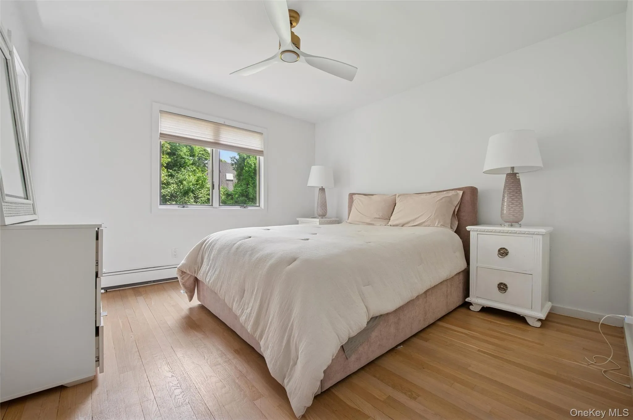 Bedroom with baseboard heating, light wood-style flooring, a ceiling fan, and baseboards Bedroom with baseboard heating, light wood-style flooring, a ceiling fan, and baseboards