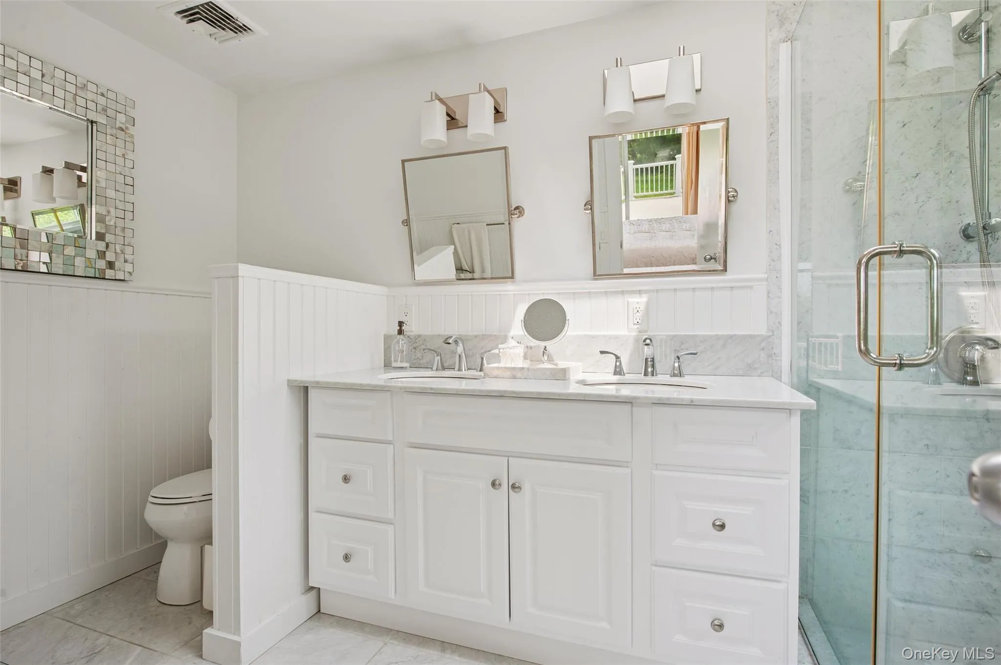 Bathroom featuring wainscoting, toilet, a shower stall, and double vanity Bathroom featuring wainscoting, toilet, a shower stall, and double vanity