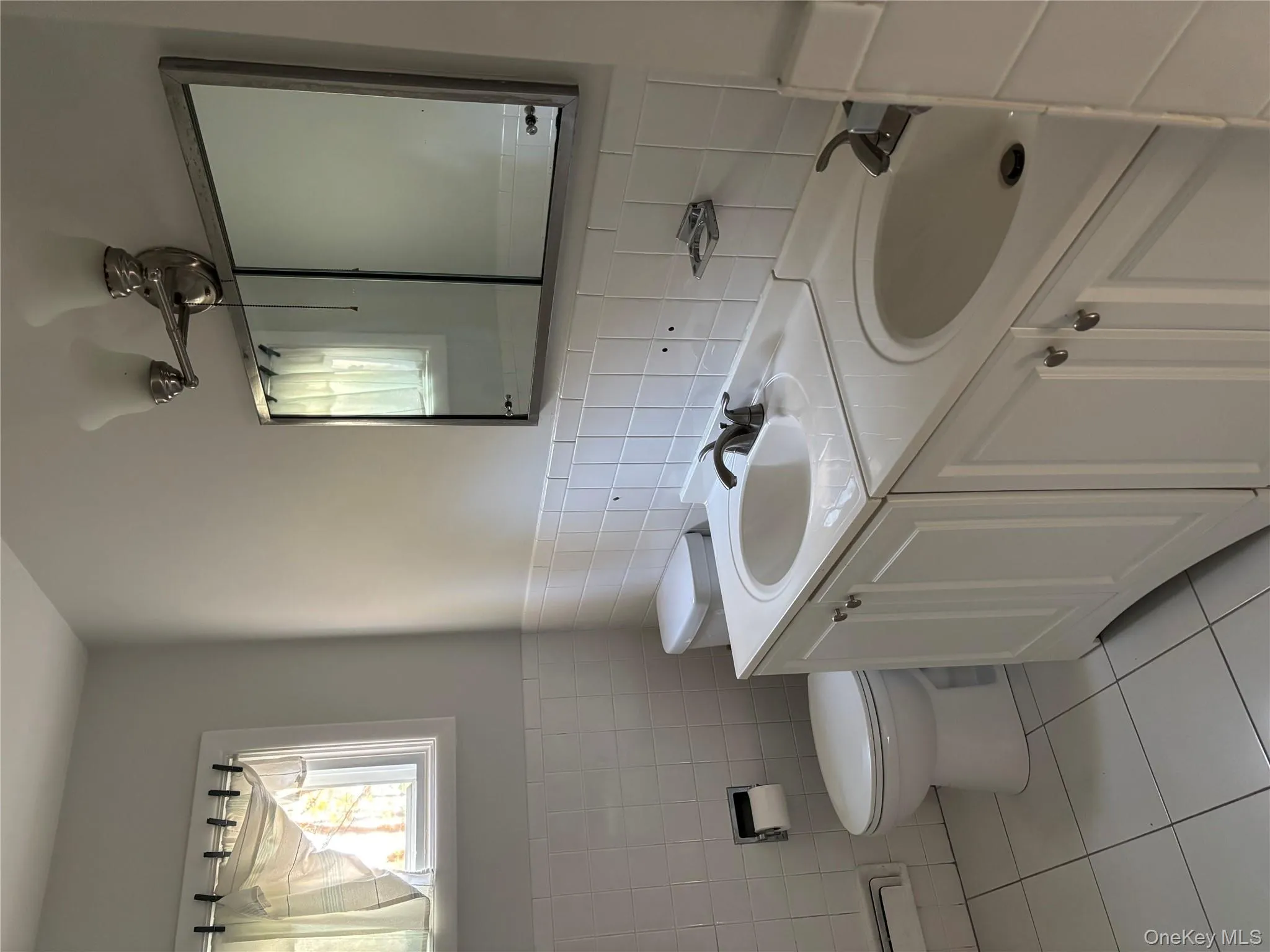 Full bathroom with tile walls, light tile patterned flooring, double vanity, and a wainscoted wall Full bathroom with tile walls, light tile patterned flooring, double vanity, and a wainscoted wall