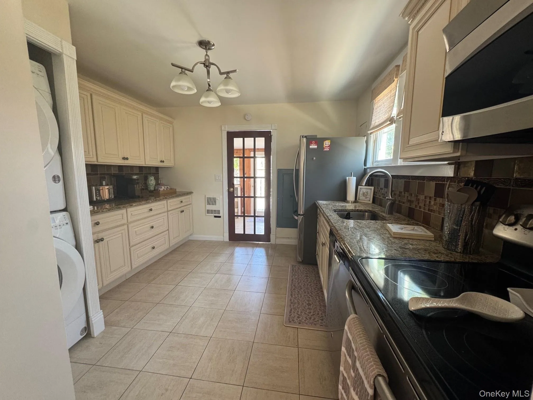 Kitchen featuring stacked washer / drying machine, appliances with stainless steel finishes, a sink, backsplash, and dark stone countertops Kitchen featuring stacked washer / drying machine, appliances with stainless steel finishes, a sink, backsplash, and dark stone countertops