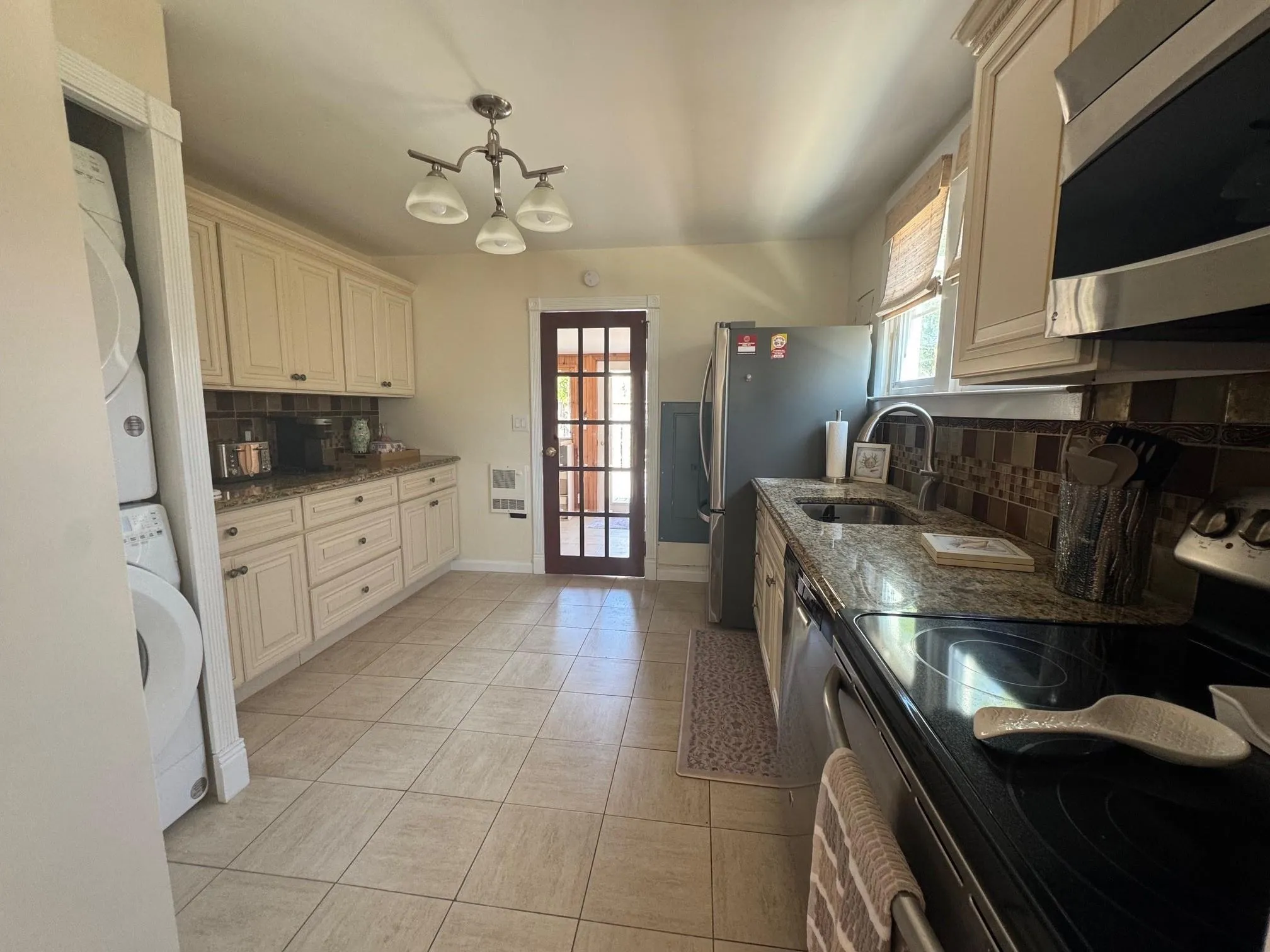 Kitchen featuring stacked washer / drying machine, appliances with stainless steel finishes, a sink, backsplash, and dark stone countertops Kitchen featuring stacked washer / drying machine, appliances with stainless steel finishes, a sink, backsplash, and dark stone countertops