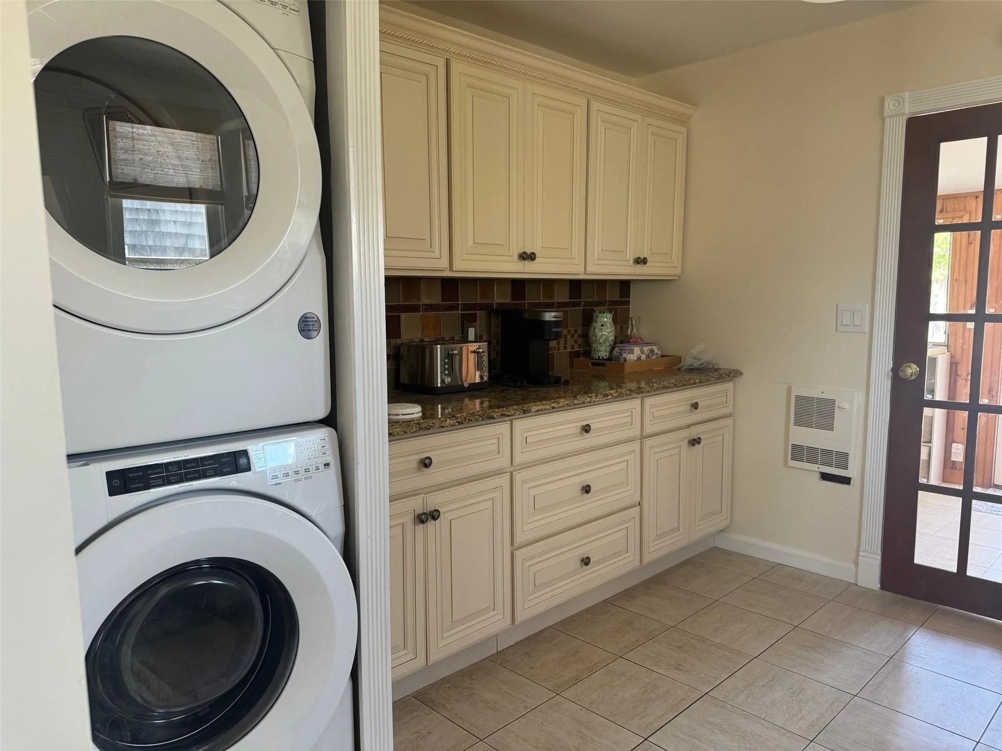 Washroom featuring stacked washer / drying machine, heating unit, light tile patterned flooring, and baseboards Washroom featuring stacked washer / drying machine, heating unit, light tile patterned flooring, and baseboards