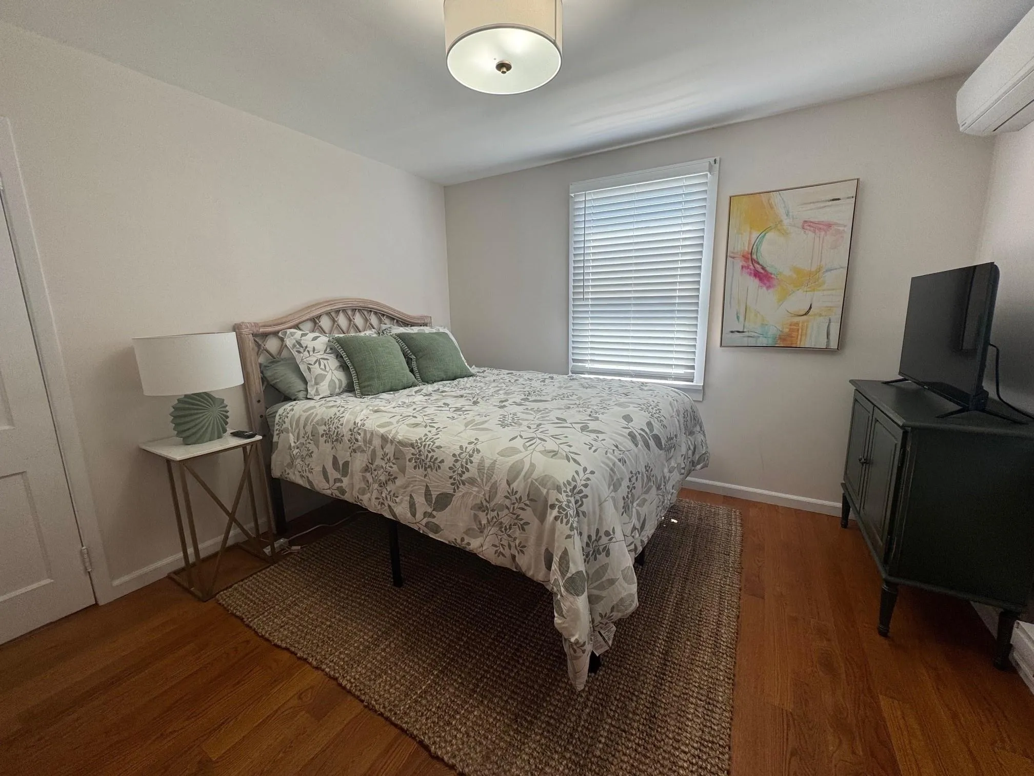 Bedroom with a wall mounted air conditioner, wood finished floors, and baseboards Bedroom with a wall mounted air conditioner, wood finished floors, and baseboards
