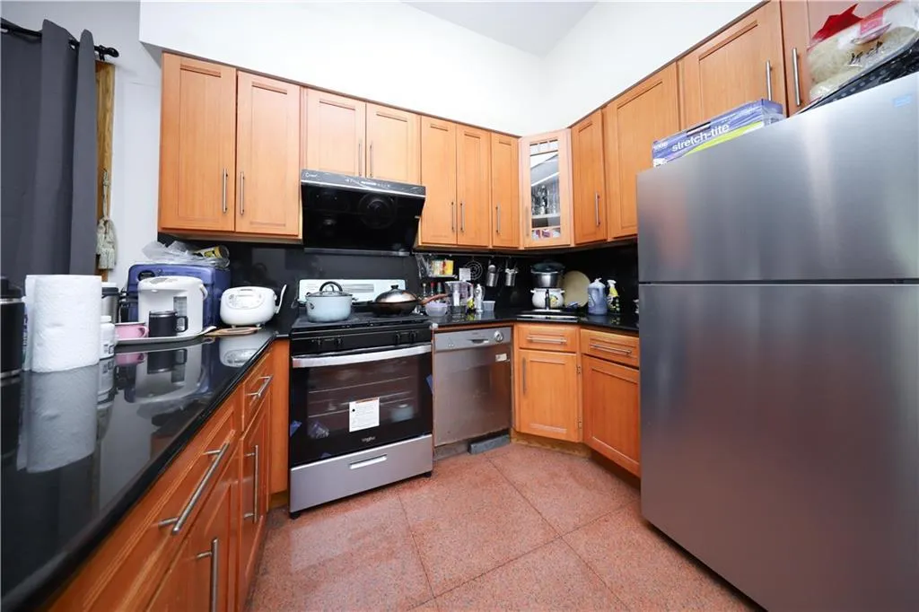Kitchen featuring appliances with stainless steel finishes, dark aggregate flooring, extractor fan, glass insert cabinets, and brown cabinets Kitchen featuring appliances with stainless steel finishes, dark aggregate flooring, extractor fan, glass insert cabinets, and brown cabinets