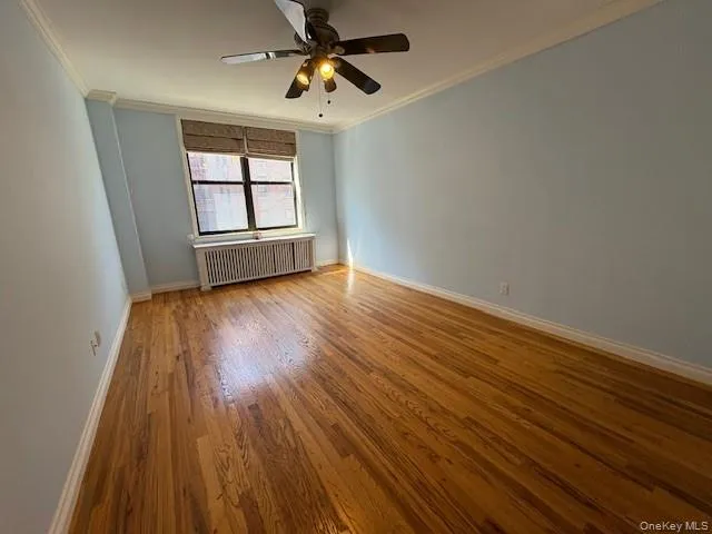 Empty room featuring wood finished floors, crown molding, radiator, and a ceiling fan Empty room featuring wood finished floors, crown molding, radiator, and a ceiling fan