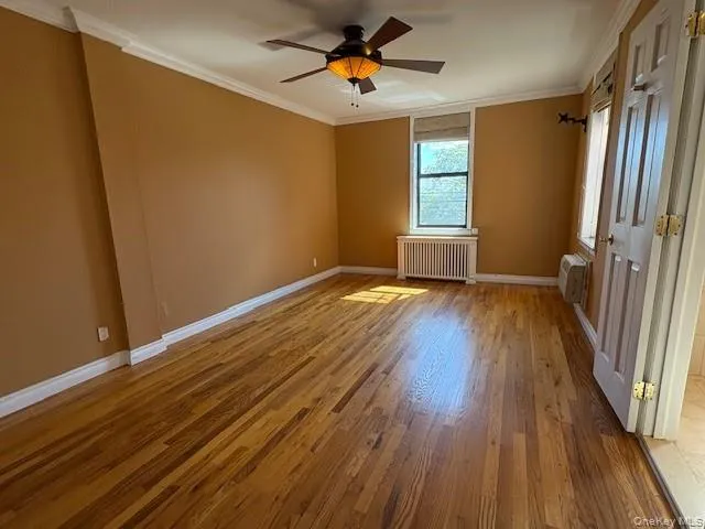 Unfurnished room featuring ornamental molding, light wood-style floors, radiator heating unit, ceiling fan, and a wall unit AC Unfurnished room featuring ornamental molding, light wood-style floors, radiator heating unit, ceiling fan, and a wall unit AC