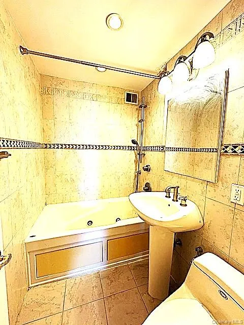 Full bathroom featuring tile walls, a combined bath / shower with jetted tub, and light tile patterned flooring Full bathroom featuring tile walls, a combined bath / shower with jetted tub, and light tile patterned flooring