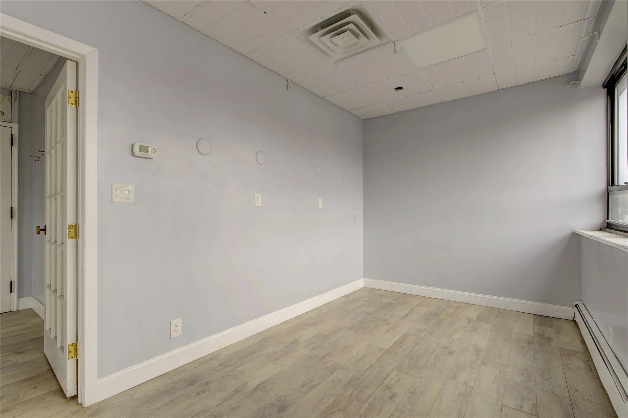 Unfurnished room with a baseboard radiator, light wood-type flooring, and baseboards Unfurnished room with a baseboard radiator, light wood-type flooring, and baseboards