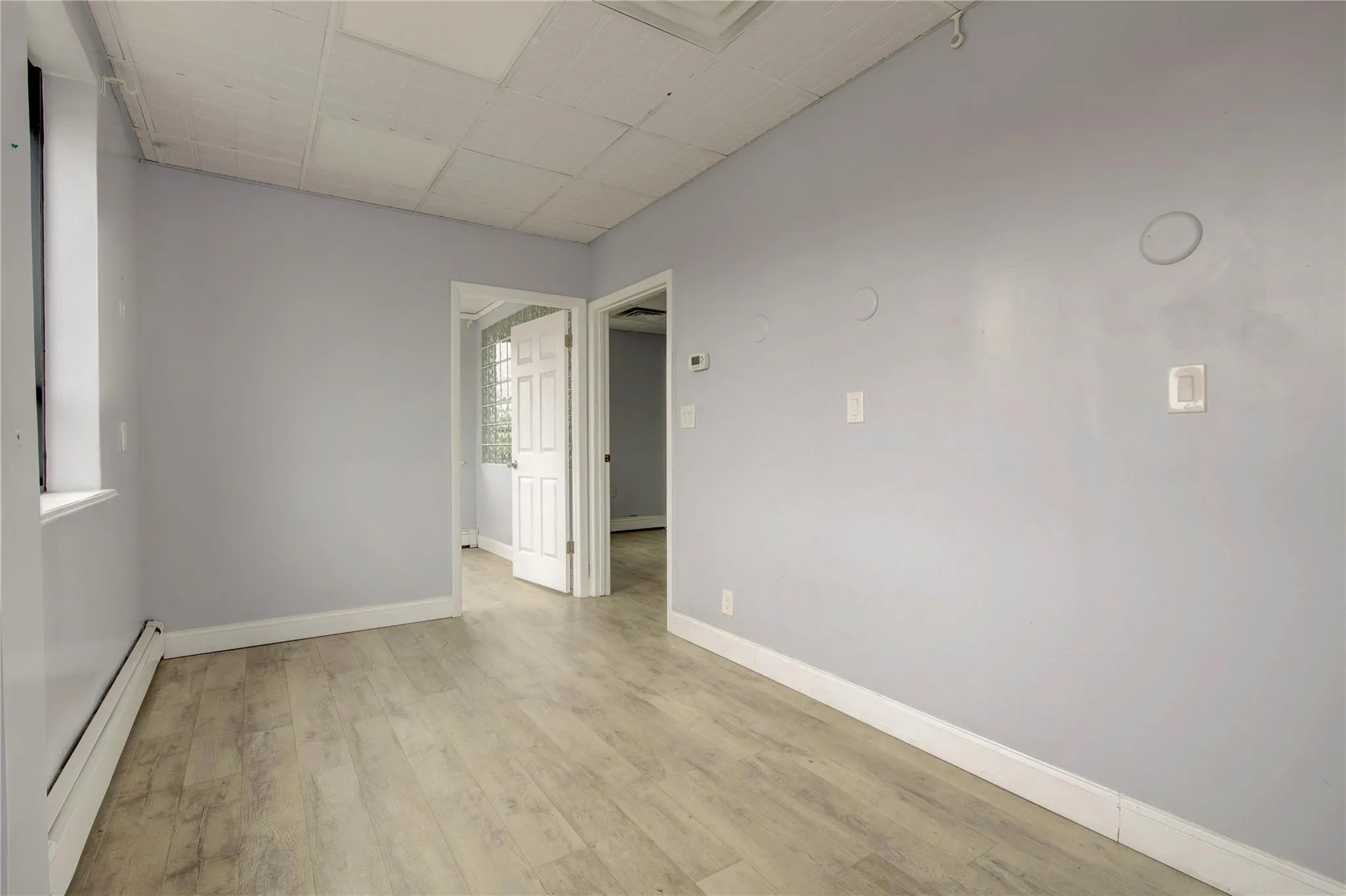 Spare room with a baseboard radiator, baseboards, light wood-style floors, and a paneled ceiling Spare room with a baseboard radiator, baseboards, light wood-style floors, and a paneled ceiling