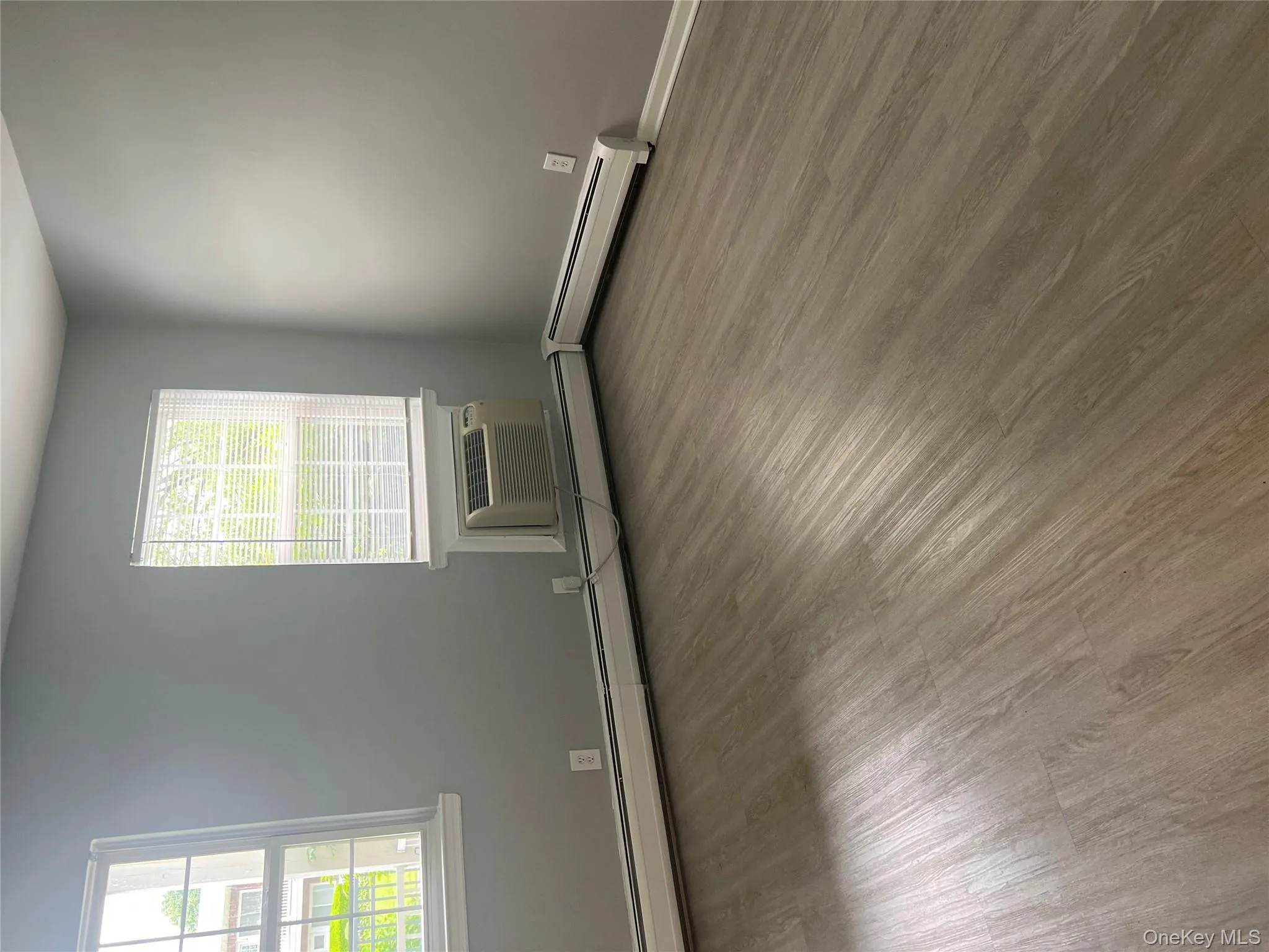 Unfurnished room with a wall mounted air conditioner, wood finished floors, and baseboards Unfurnished room with a wall mounted air conditioner, wood finished floors, and baseboards