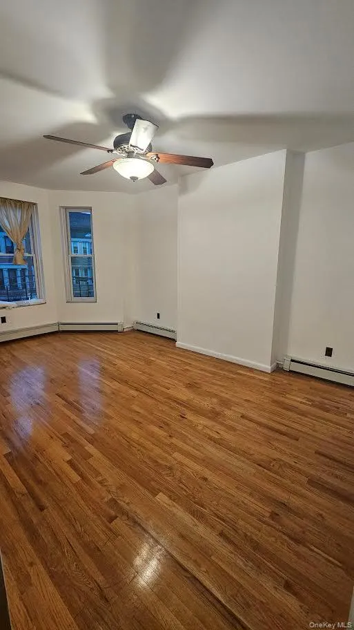 Empty room with wood finished floors, baseboard heating, a ceiling fan. Empty room with wood finished floors, baseboard heating, a ceiling fan.