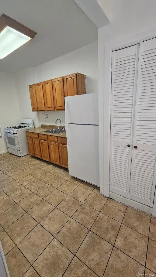 Kitchen with white appliances, a sink, brown cabinets, light countertops, and light tile patterned flooring Kitchen with white appliances, a sink, brown cabinets, light countertops, and light tile patterned flooring