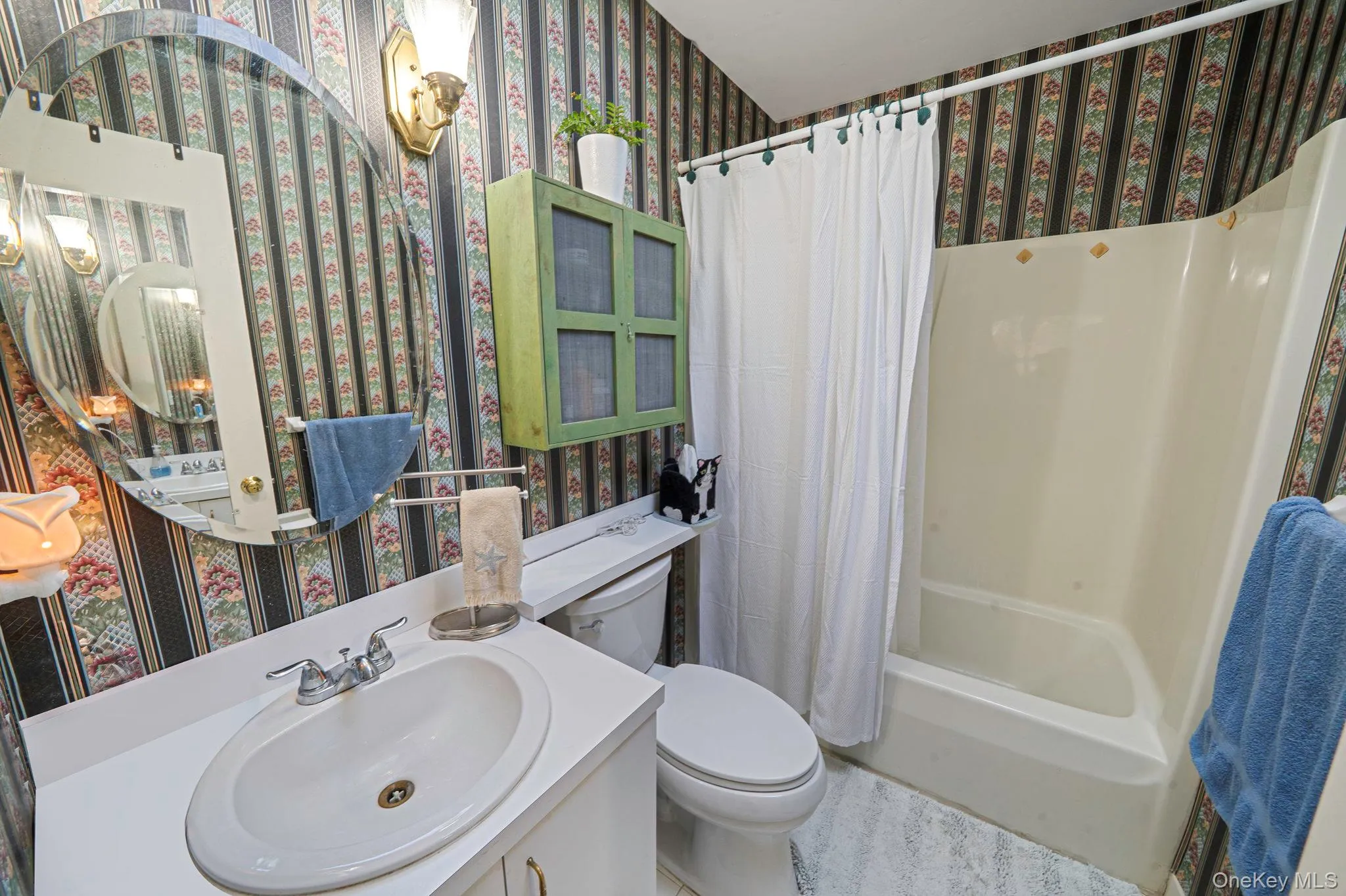 Full bathroom with wallpapered walls, toilet, shower / bath combo, and vanity Full bathroom with wallpapered walls, toilet, shower / bath combo, and vanity