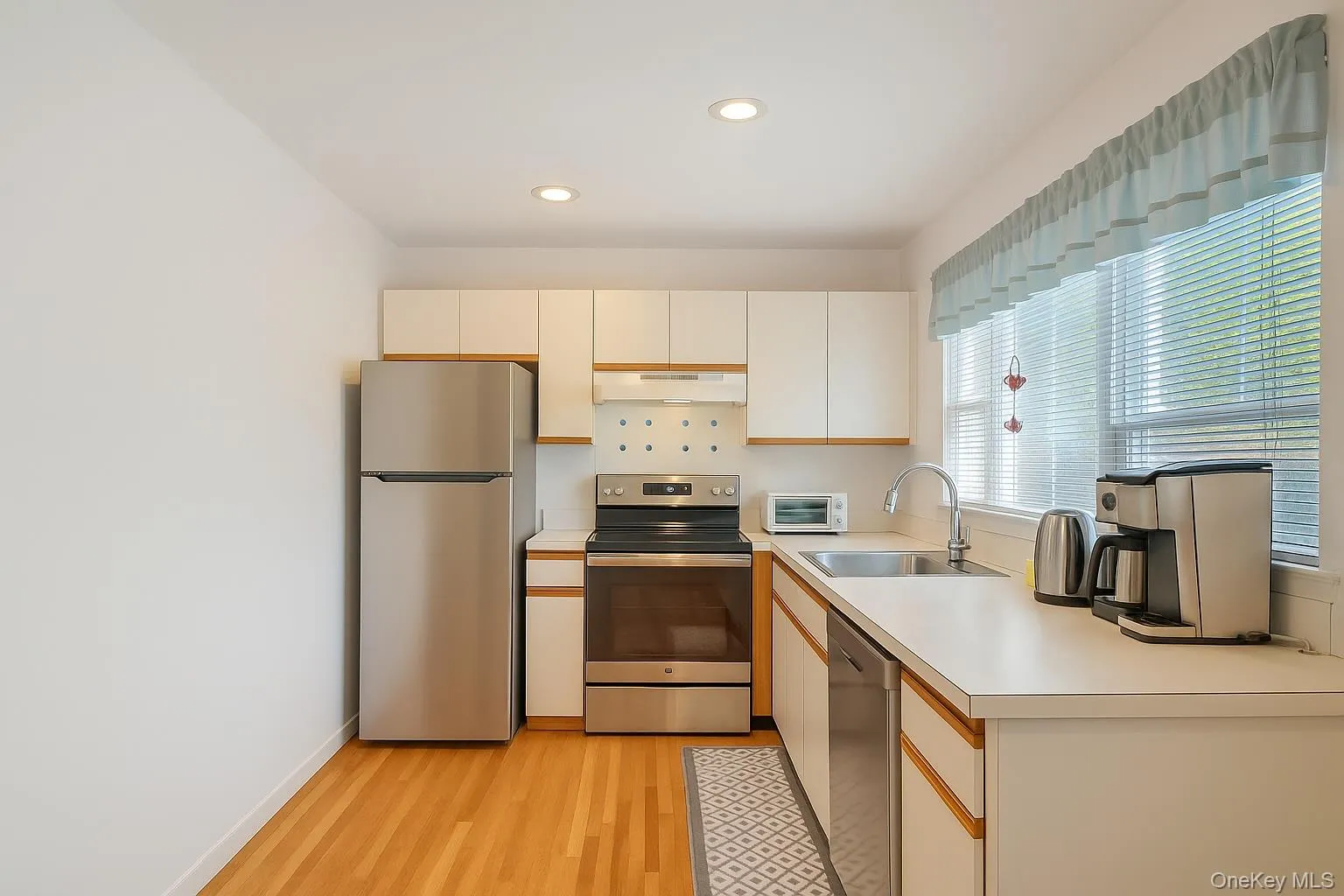 Kitchen featuring appliances with stainless steel finishes, a sink, under cabinet range hood, light wood-style floors, and light countertops Kitchen featuring appliances with stainless steel finishes, a sink, under cabinet range hood, light wood-style floors, and light countertops