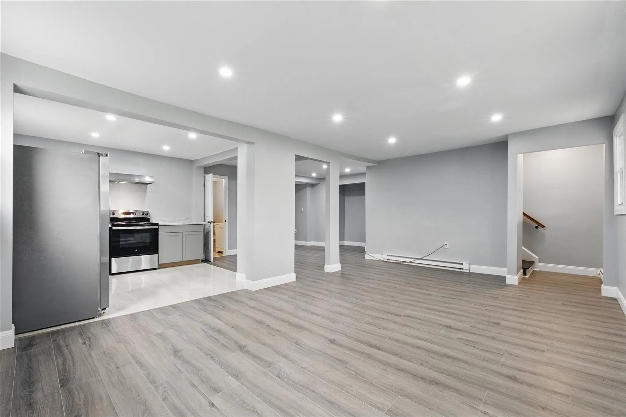 Unfurnished living room with a baseboard radiator, light wood finished floors, baseboards, recessed lighting, and stairway Unfurnished living room with a baseboard radiator, light wood finished floors, baseboards, recessed lighting, and stairway