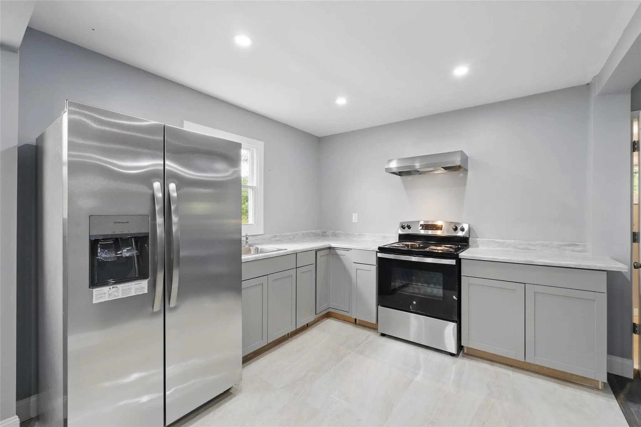 Kitchen with appliances with stainless steel finishes, wall chimney range hood, gray cabinetry, light countertops, and recessed lighting Kitchen with appliances with stainless steel finishes, wall chimney range hood, gray cabinetry, light countertops, and recessed lighting
