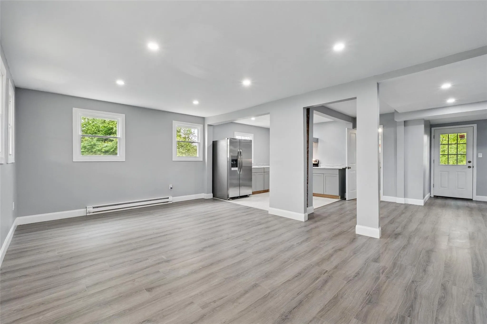 Unfurnished living room with a baseboard radiator, recessed lighting, baseboards, light wood-style floors, and healthy amount of natural light Unfurnished living room with a baseboard radiator, recessed lighting, baseboards, light wood-style floors, and healthy amount of natural light