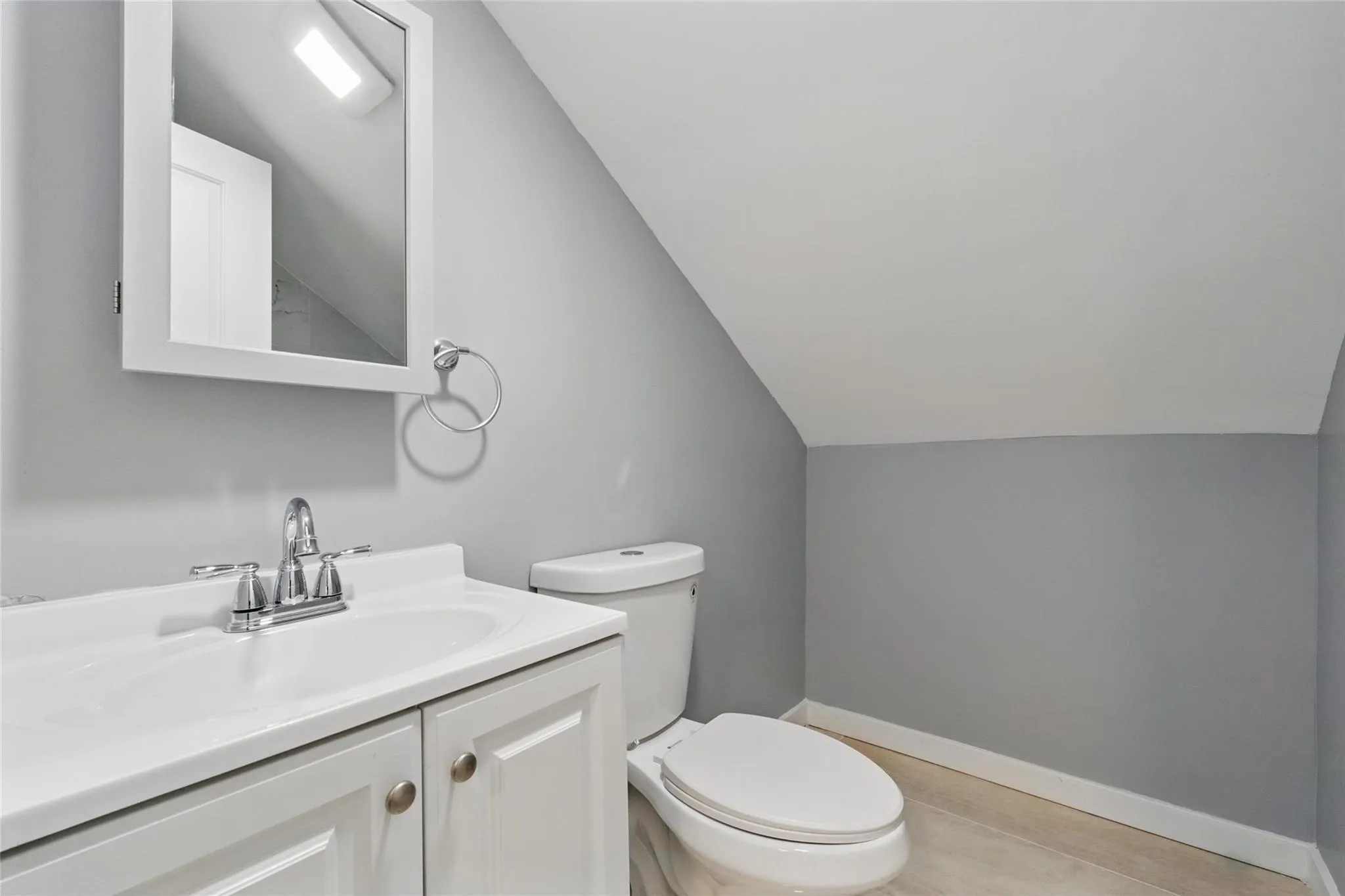 Half bath featuring vaulted ceiling, toilet, vanity, and baseboards Half bath featuring vaulted ceiling, toilet, vanity, and baseboards