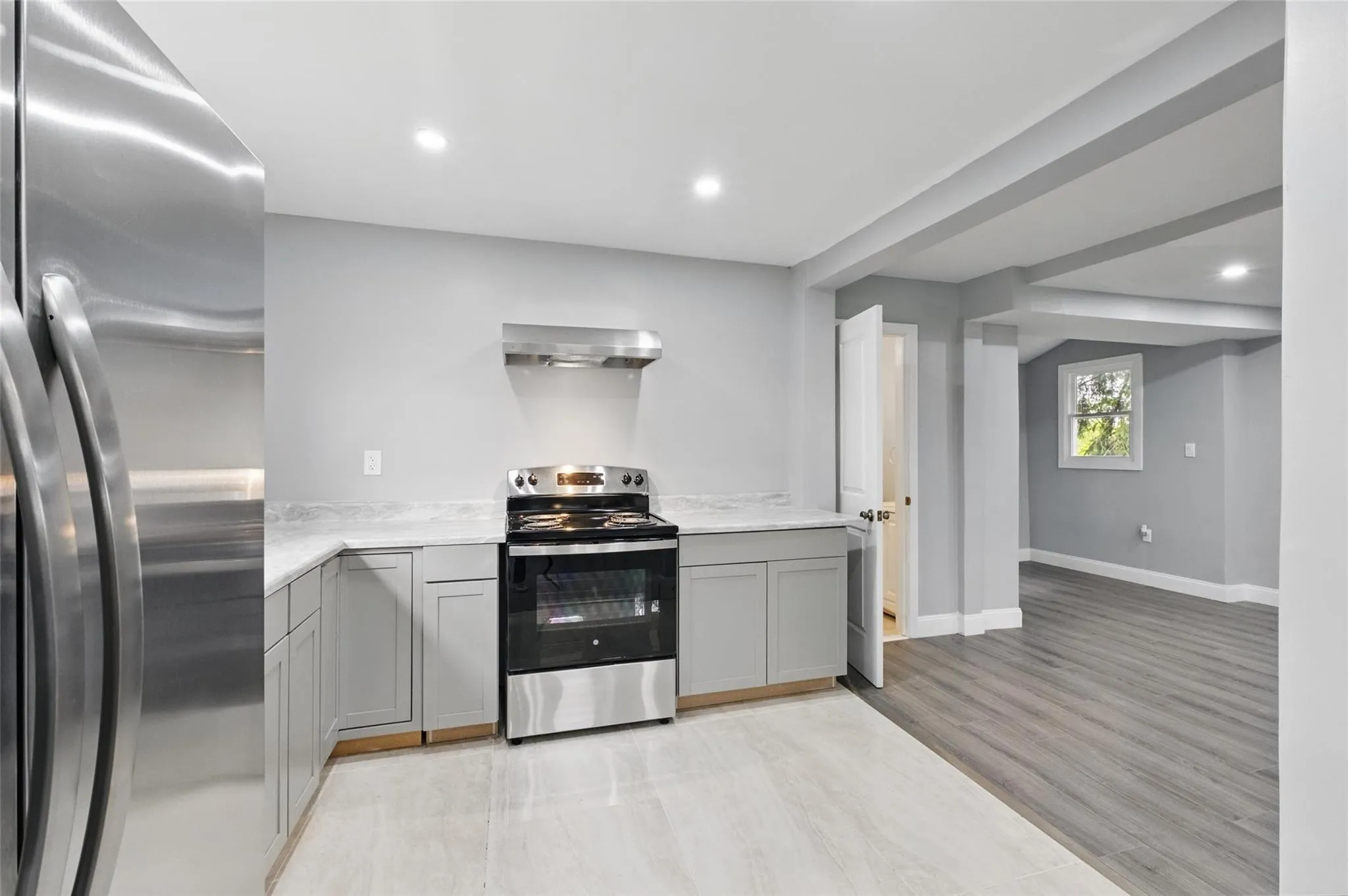 Kitchen featuring appliances with stainless steel finishes, wall chimney range hood, gray cabinetry, recessed lighting, and baseboards Kitchen featuring appliances with stainless steel finishes, wall chimney range hood, gray cabinetry, recessed lighting, and baseboards