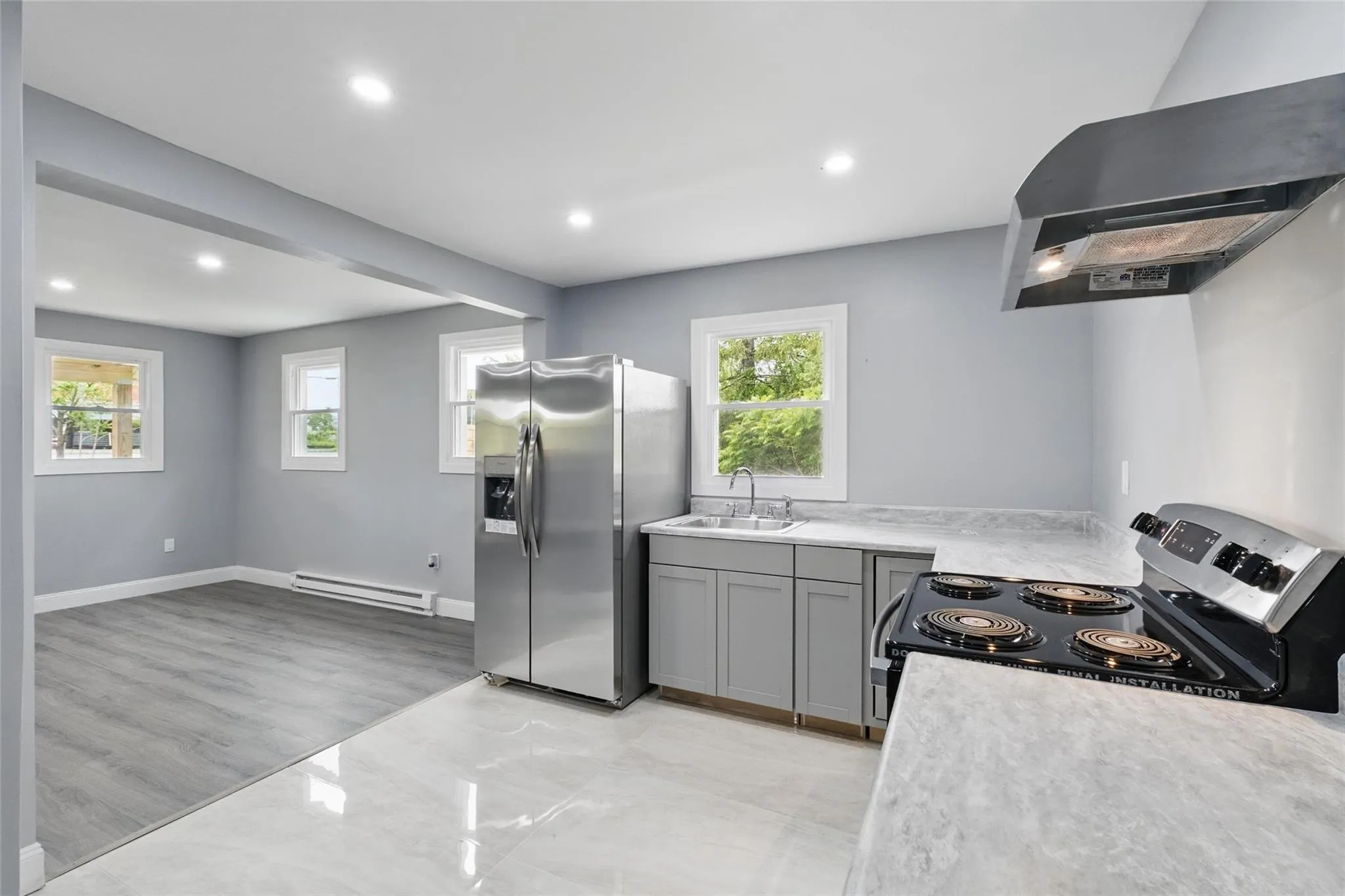 Kitchen with stainless steel appliances, wall chimney exhaust hood, a sink, baseboard heating, and light countertops Kitchen with stainless steel appliances, wall chimney exhaust hood, a sink, baseboard heating, and light countertops