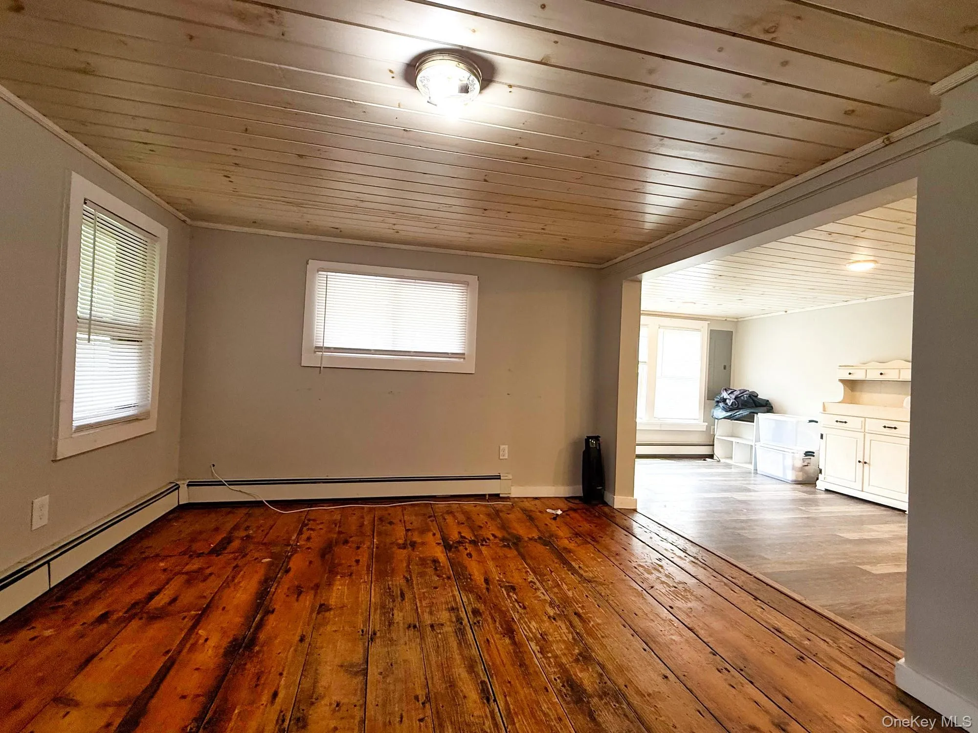 Unfurnished living room with wood ceiling, wood-type flooring, crown molding, and baseboard heating Unfurnished living room with wood ceiling, wood-type flooring, crown molding, and baseboard heating