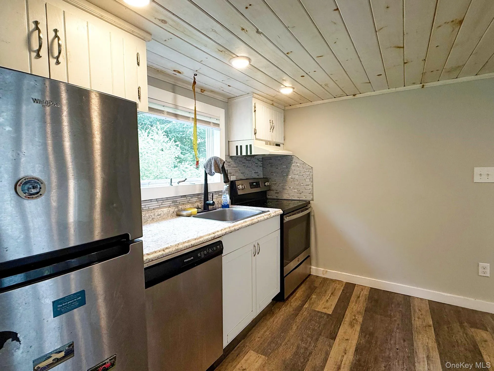 Kitchen with stainless steel appliances, decorative backsplash, wood ceiling, dark wood-style floors, and light countertops Kitchen with stainless steel appliances, decorative backsplash, wood ceiling, dark wood-style floors, and light countertops