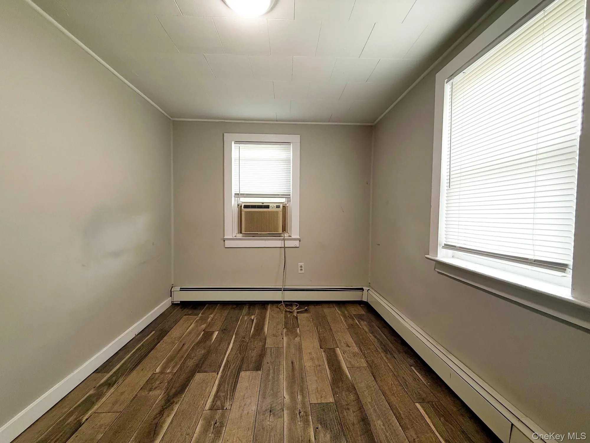 Spare room with baseboard heating, dark wood-type flooring, and cooling unit Spare room with baseboard heating, dark wood-type flooring, and cooling unit