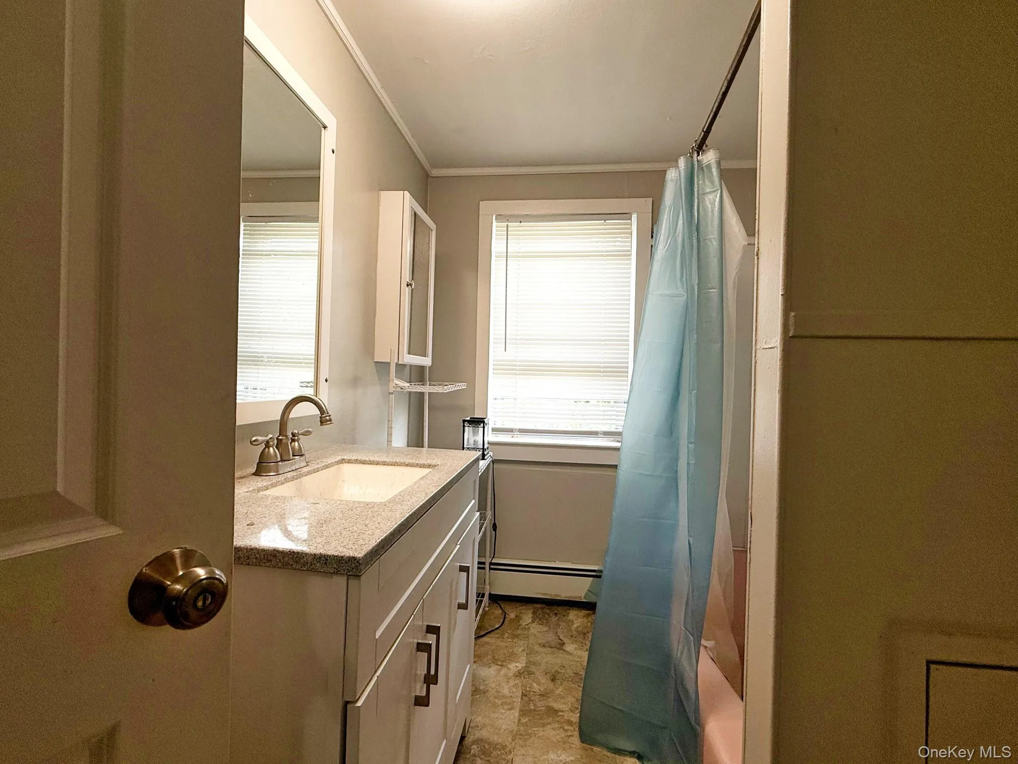 Full bath featuring ornamental molding, vanity, a baseboard heating unit, plenty of natural light, and shower / tub combo with curtain Full bath featuring ornamental molding, vanity, a baseboard heating unit, plenty of natural light, and shower / tub combo with curtain