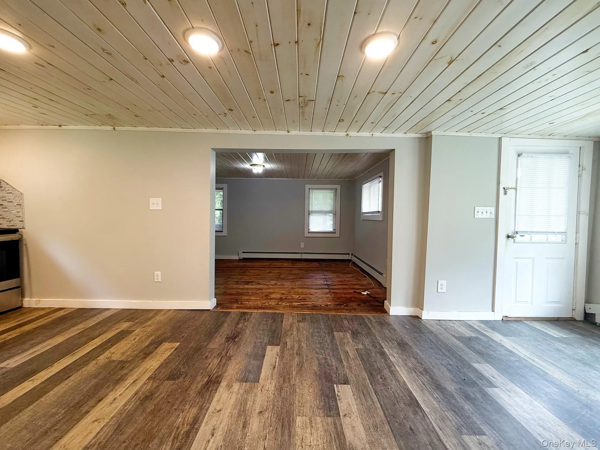 Unfurnished living room with wooden ceiling, wood finished floors, and baseboard heating Unfurnished living room with wooden ceiling, wood finished floors, and baseboard heating