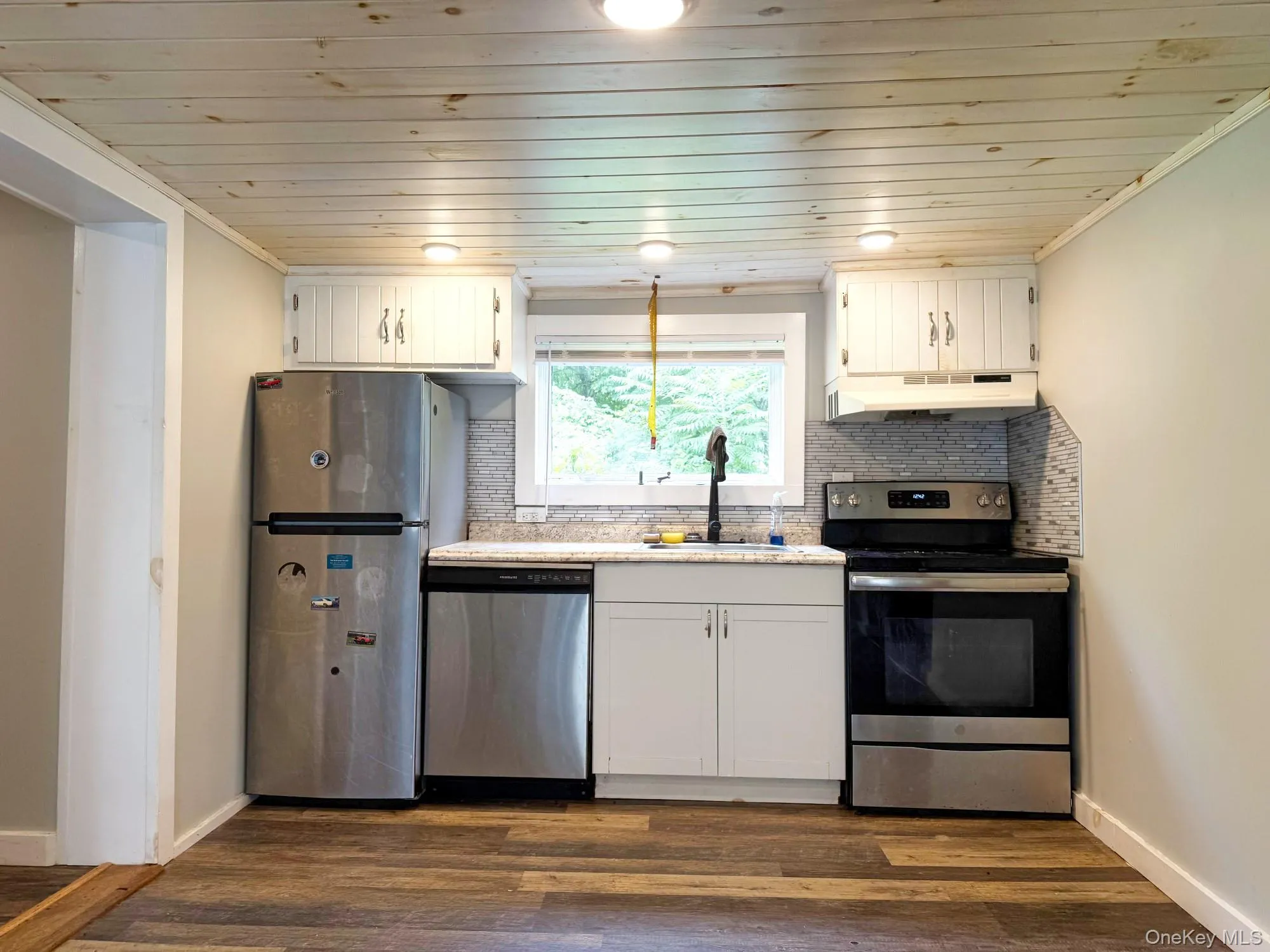 Kitchen featuring stainless steel appliances, under cabinet range hood, backsplash, wooden ceiling, and white cabinetry Kitchen featuring stainless steel appliances, under cabinet range hood, backsplash, wooden ceiling, and white cabinetry