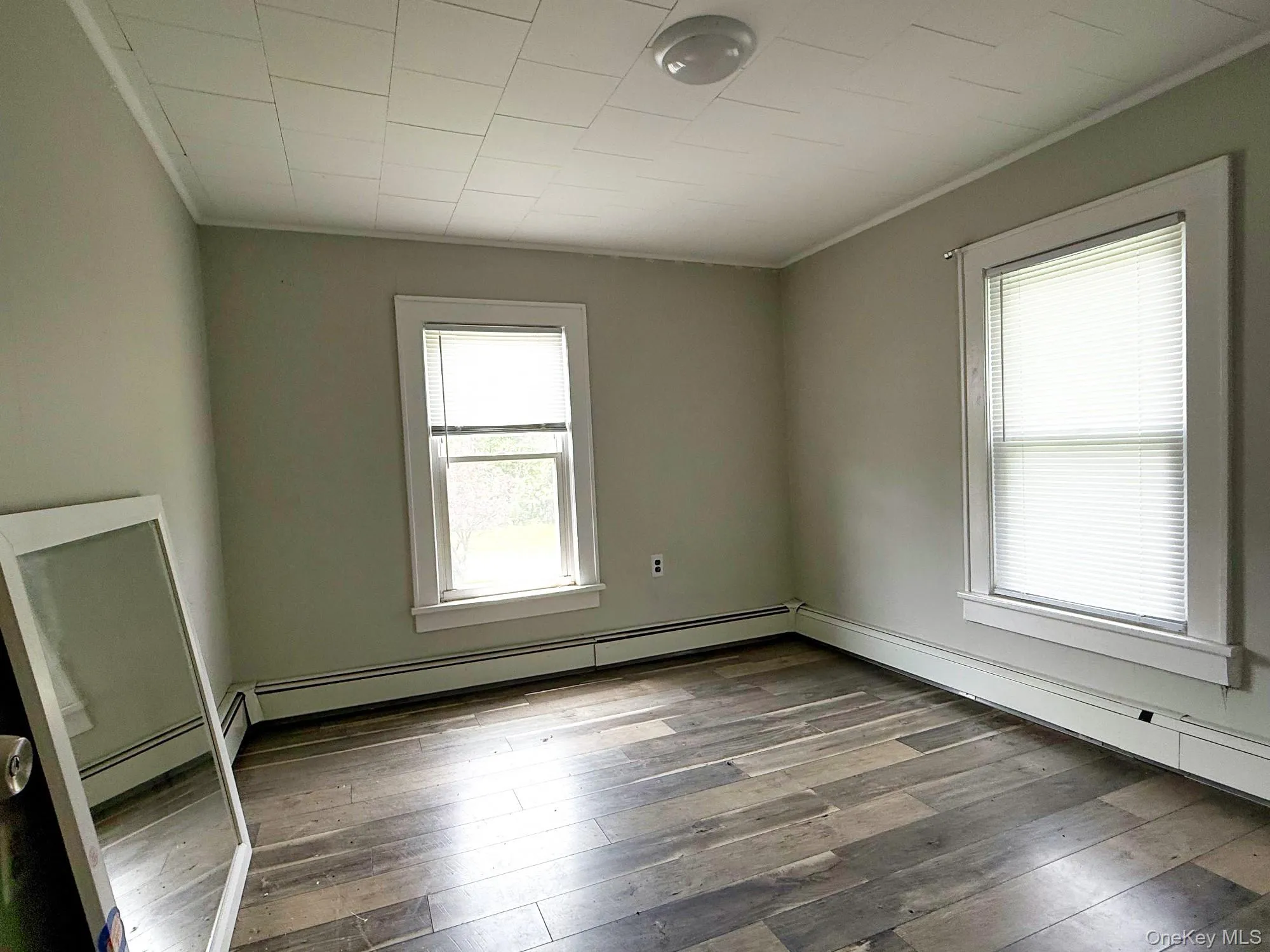 Empty room featuring crown molding, hardwood / wood-style flooring, and a baseboard heating unit Empty room featuring crown molding, hardwood / wood-style flooring, and a baseboard heating unit