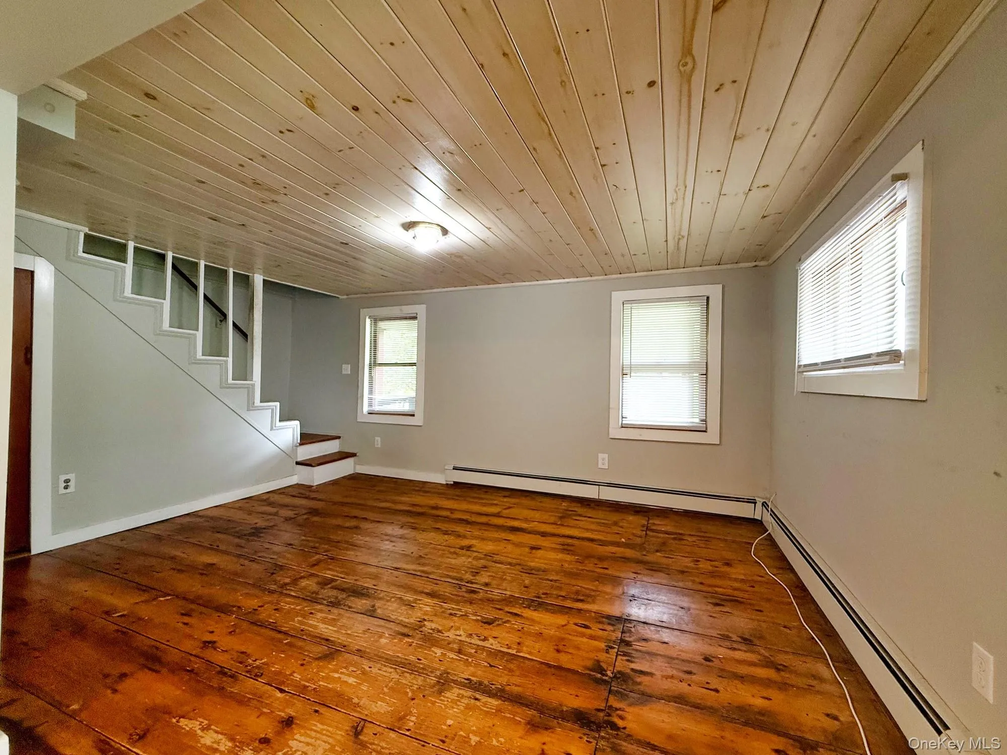 Empty room featuring wood ceiling, a baseboard radiator, stairs, and hardwood / wood-style floors Empty room featuring wood ceiling, a baseboard radiator, stairs, and hardwood / wood-style floors