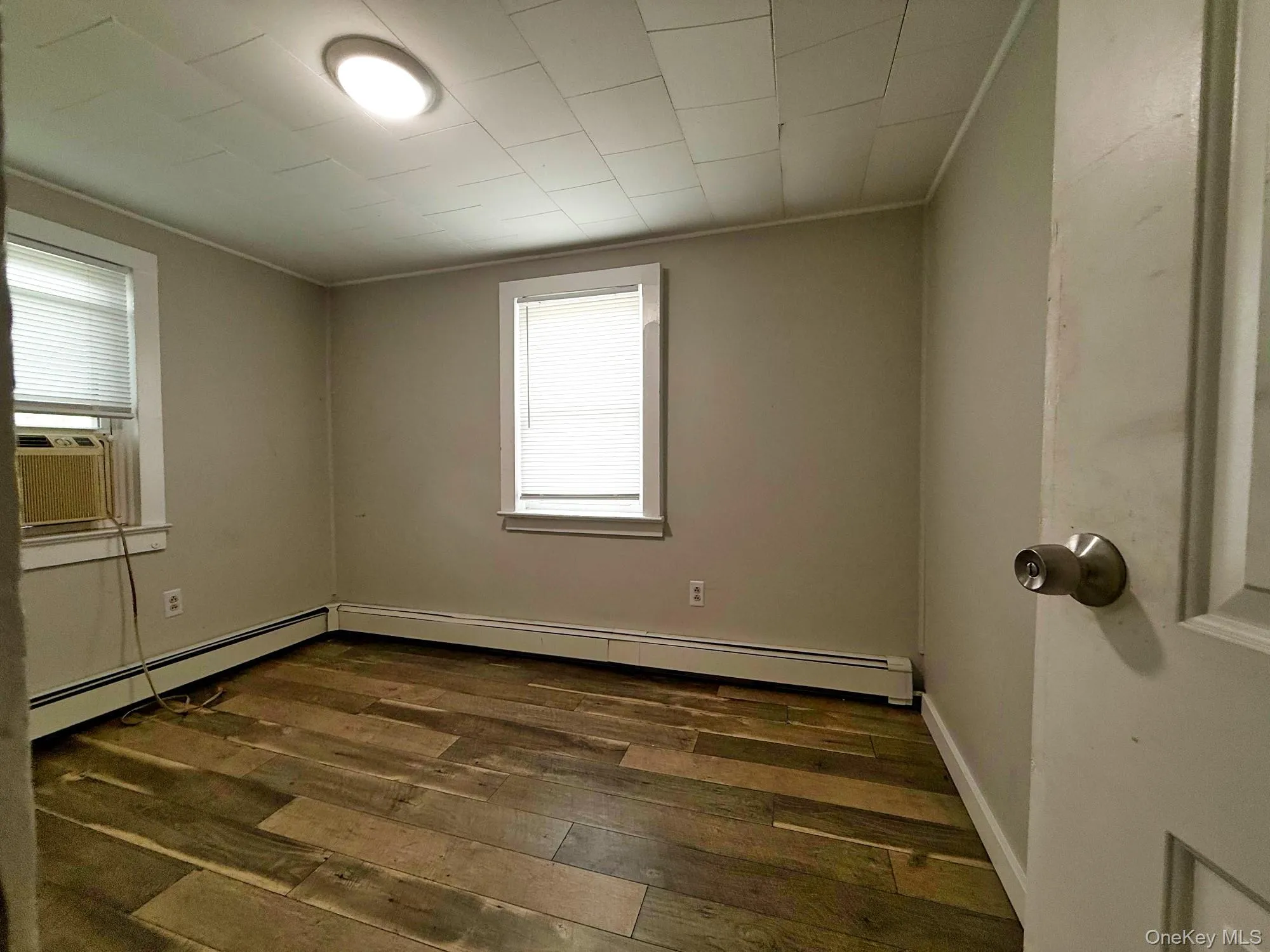 Empty room with dark wood-style flooring, baseboard heating, cooling unit, and ornamental molding Empty room with dark wood-style flooring, baseboard heating, cooling unit, and ornamental molding