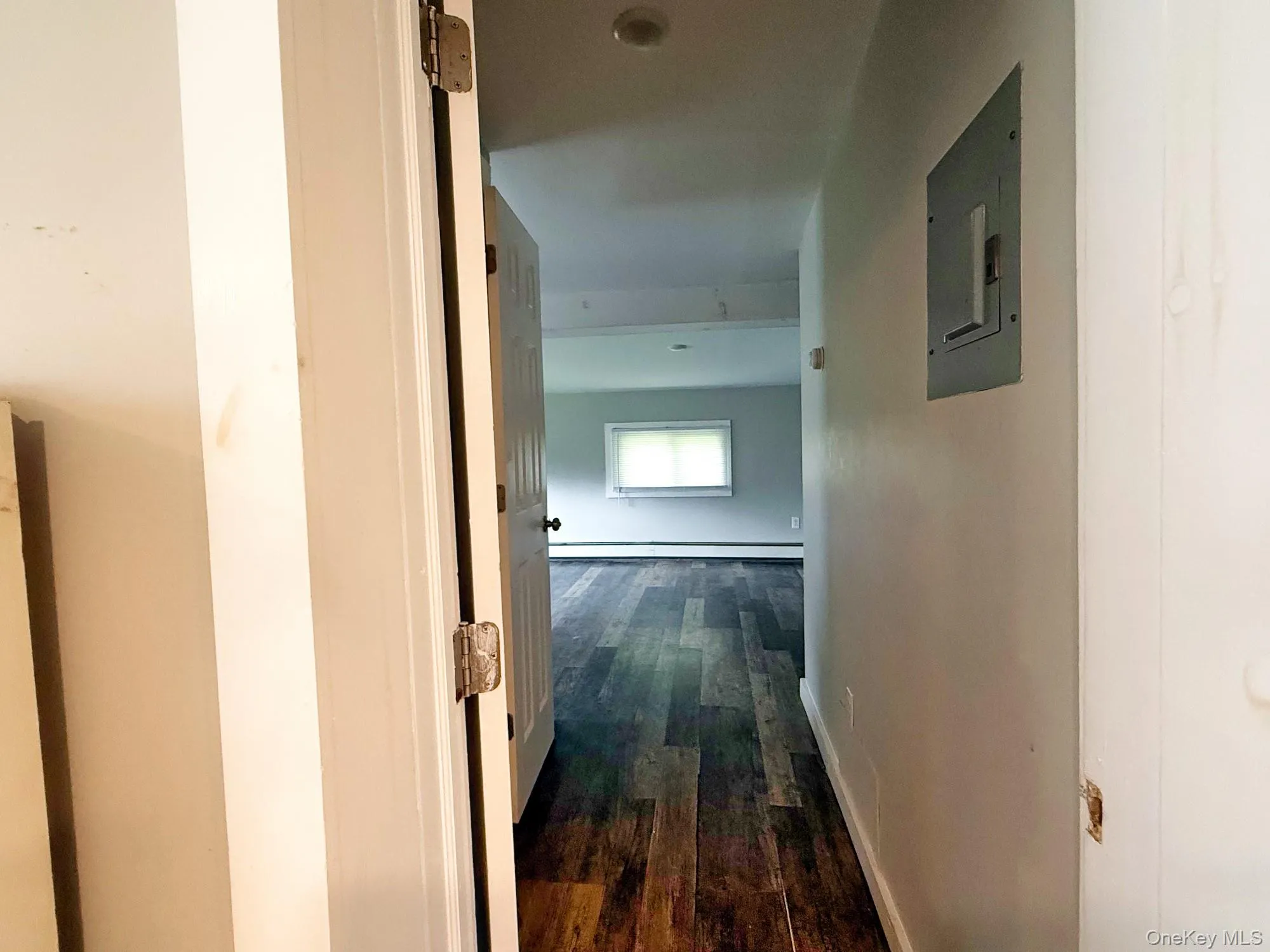 Hallway featuring electric panel, dark wood-type flooring, and a baseboard heating unit Hallway featuring electric panel, dark wood-type flooring, and a baseboard heating unit