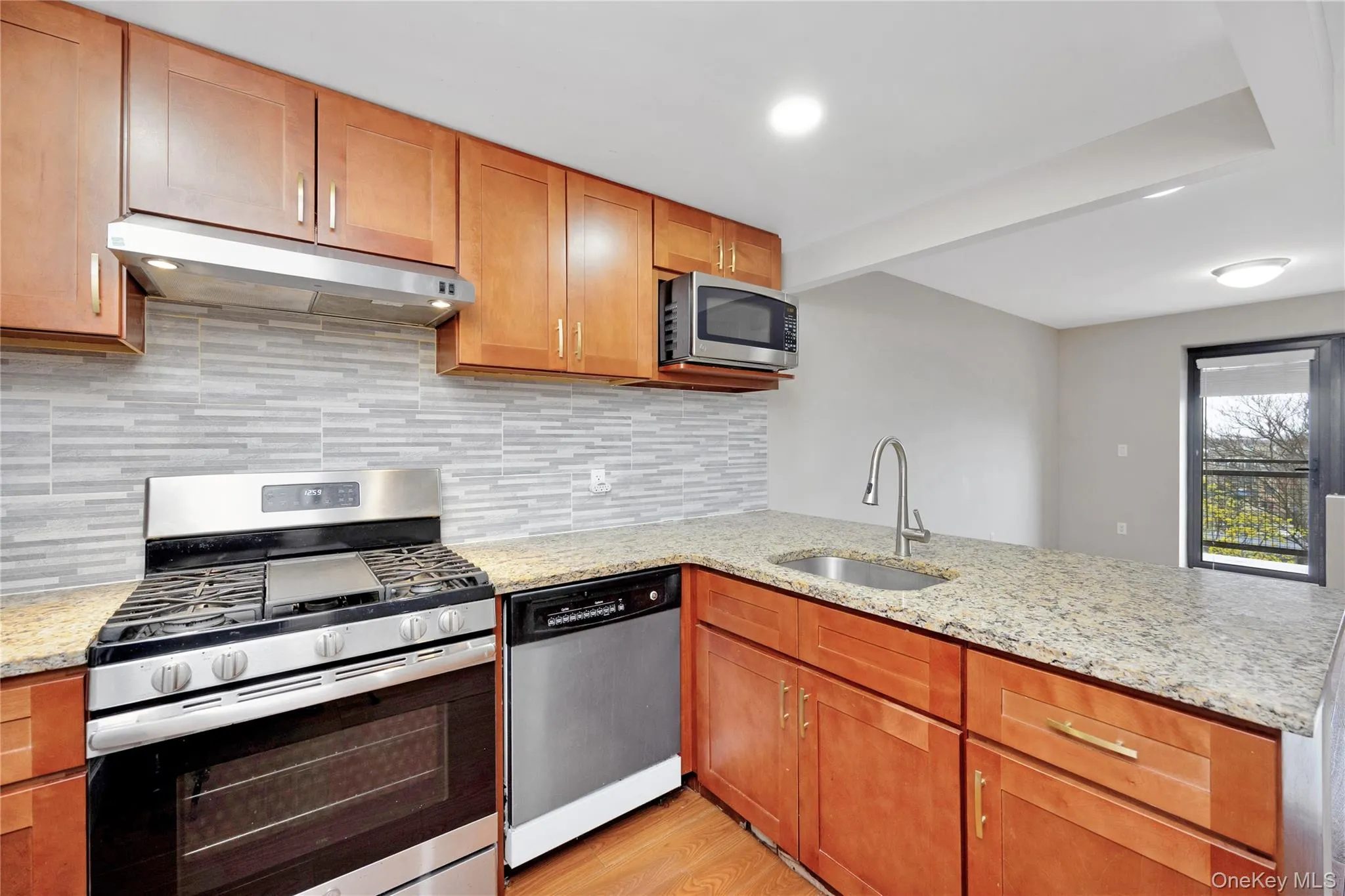 Kitchen with a peninsula, under cabinet range hood, light wood-style floors, appliances with stainless steel finishes, and a sink Kitchen with a peninsula, under cabinet range hood, light wood-style floors, appliances with stainless steel finishes, and a sink