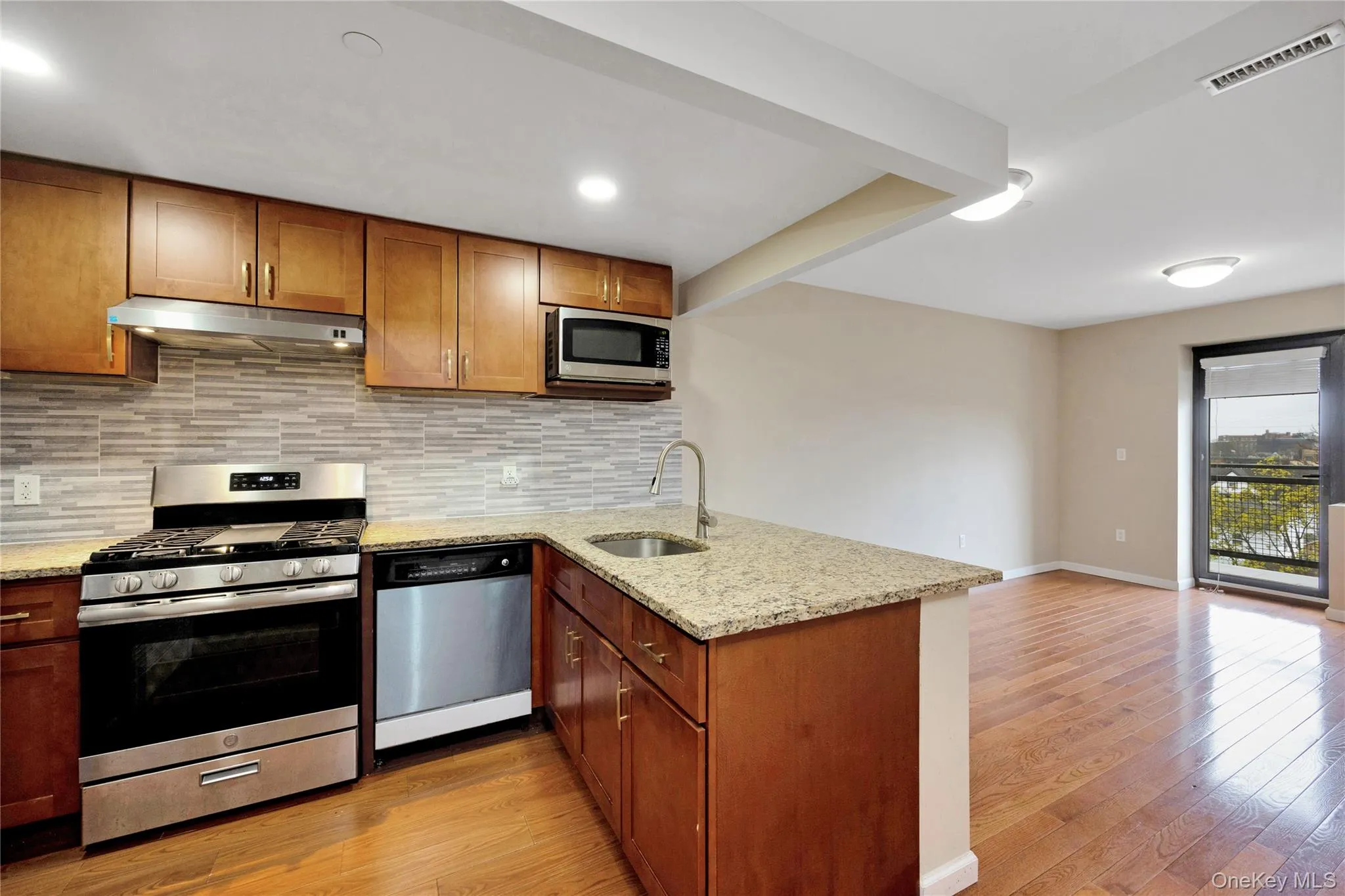 Kitchen featuring a peninsula, visible vents, appliances with stainless steel finishes, under cabinet range hood, and a sink Kitchen featuring a peninsula, visible vents, appliances with stainless steel finishes, under cabinet range hood, and a sink