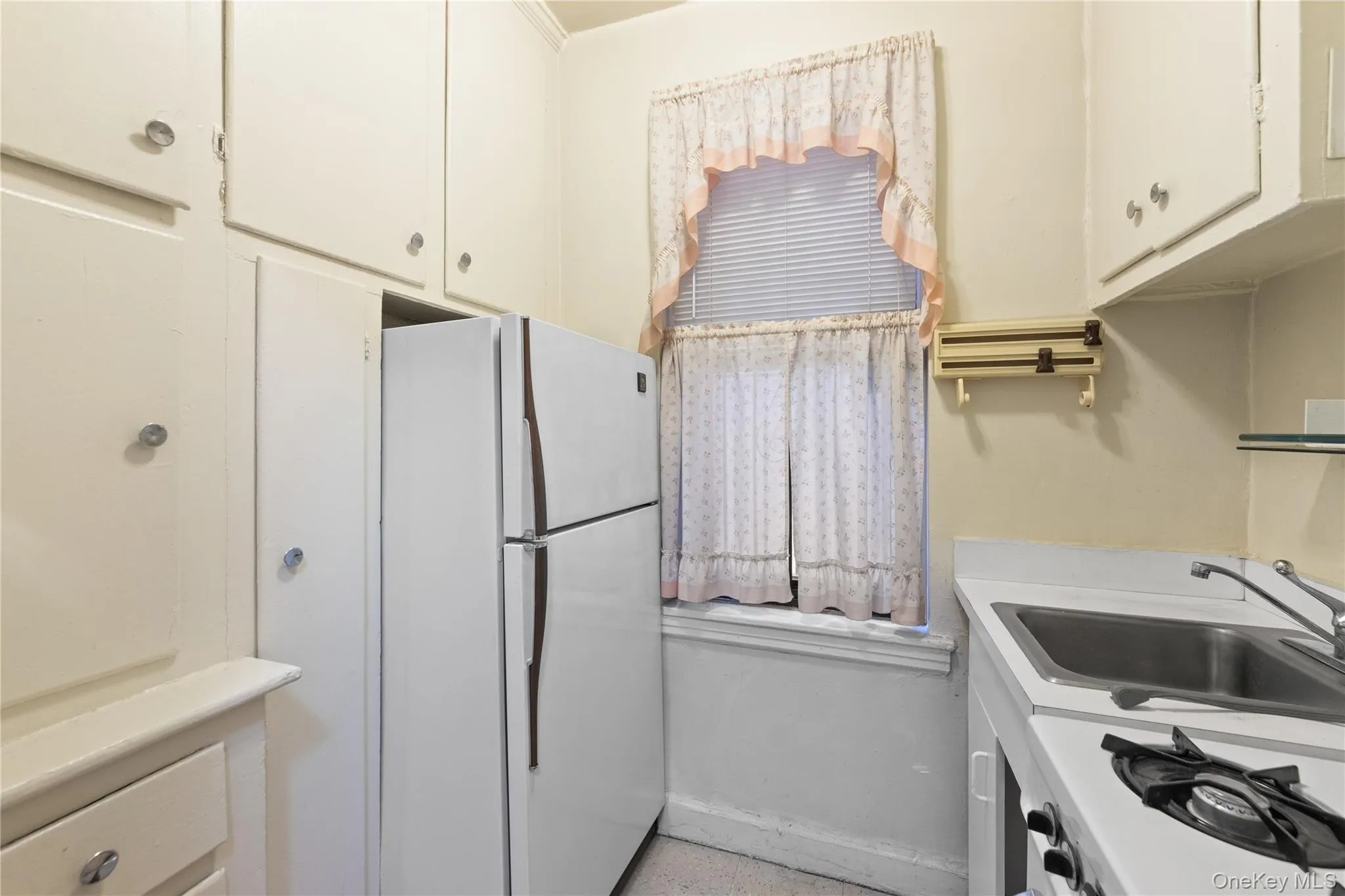 Kitchen with freestanding refrigerator, a sink, light countertops, and white cabinets Kitchen with freestanding refrigerator, a sink, light countertops, and white cabinets