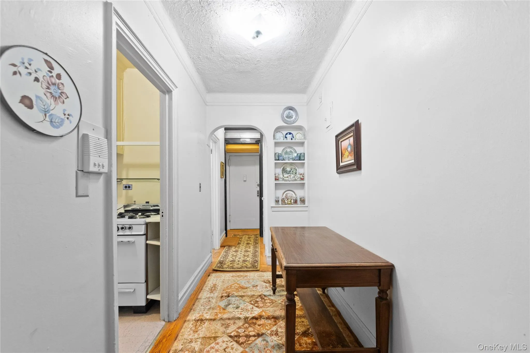 Hallway featuring a textured ceiling, built in features, crown molding, and arched walkways Hallway featuring a textured ceiling, built in features, crown molding, and arched walkways