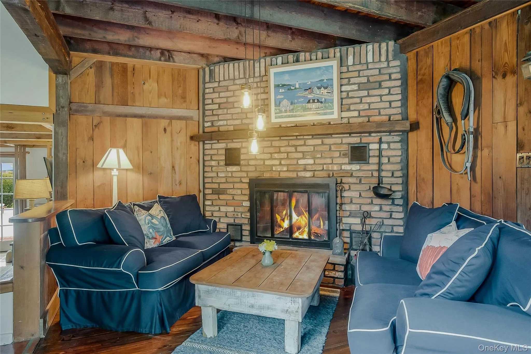 Living room featuring wood walls, wood finished floors, beam ceiling, and a fireplace Living room featuring wood walls, wood finished floors, beam ceiling, and a fireplace
